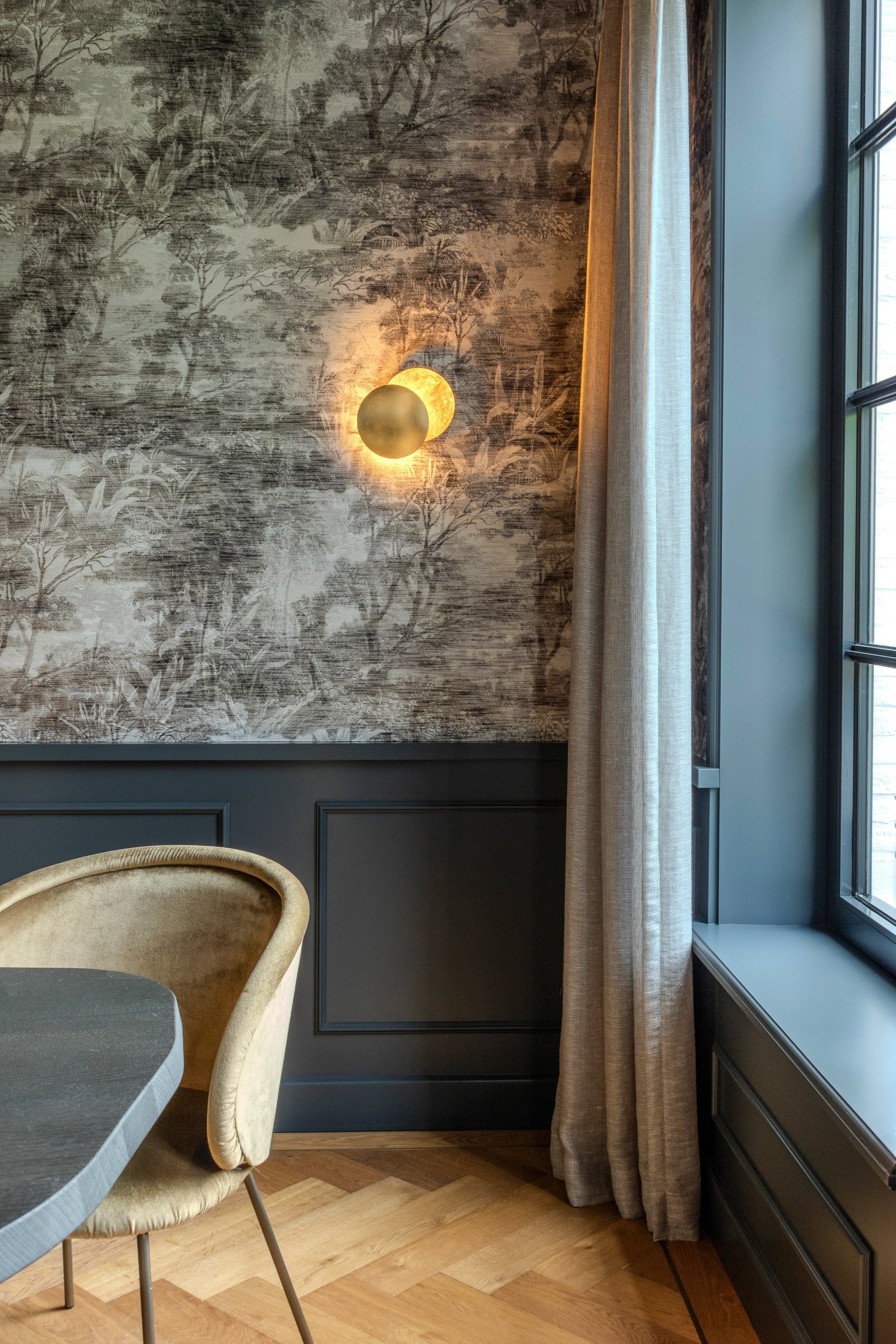Lounge area with patterned wallpaper, brass wall sconce and dark paneling