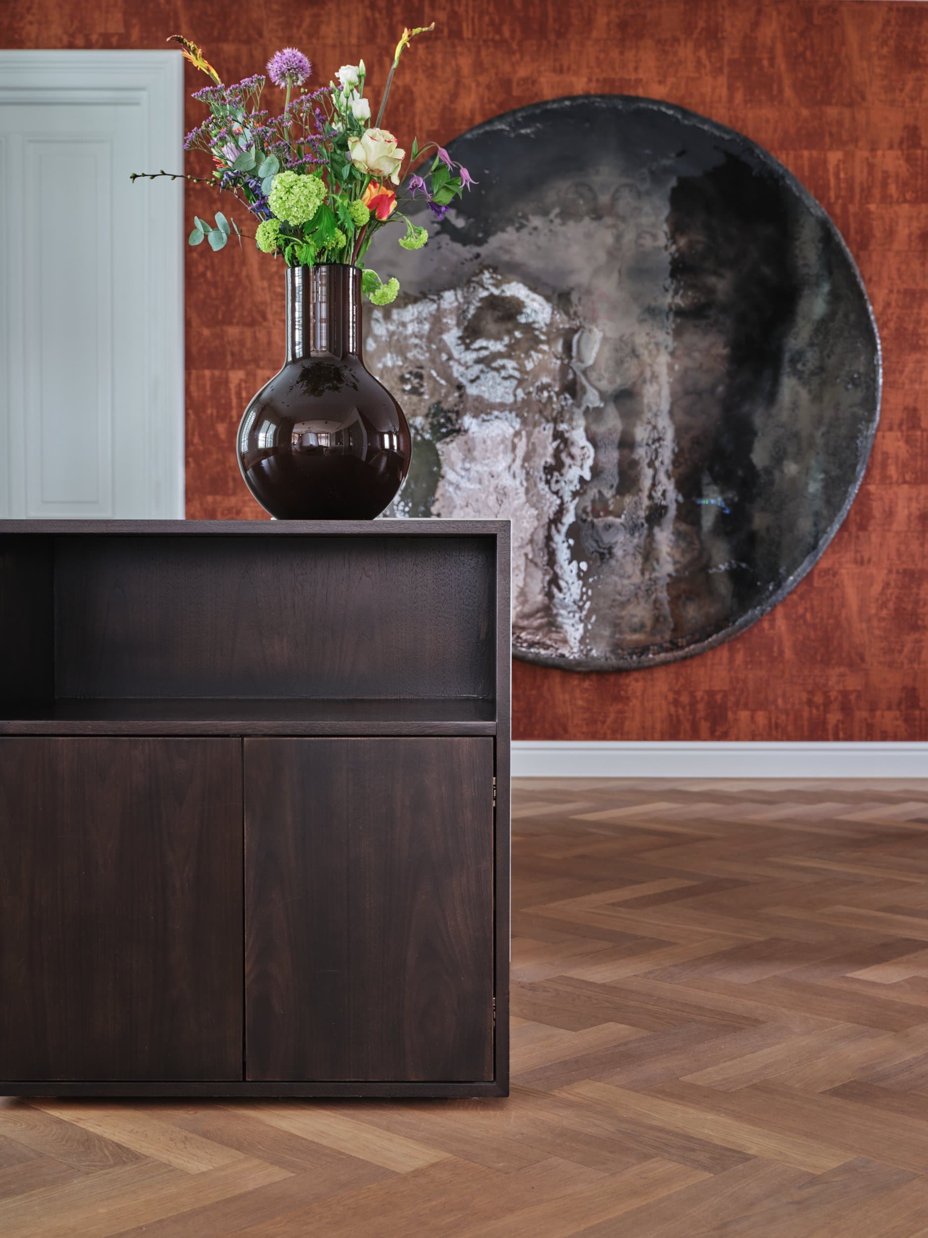 Woonkamer met zwarte stoelen, gouden tafellamp en gelijste portretfoto