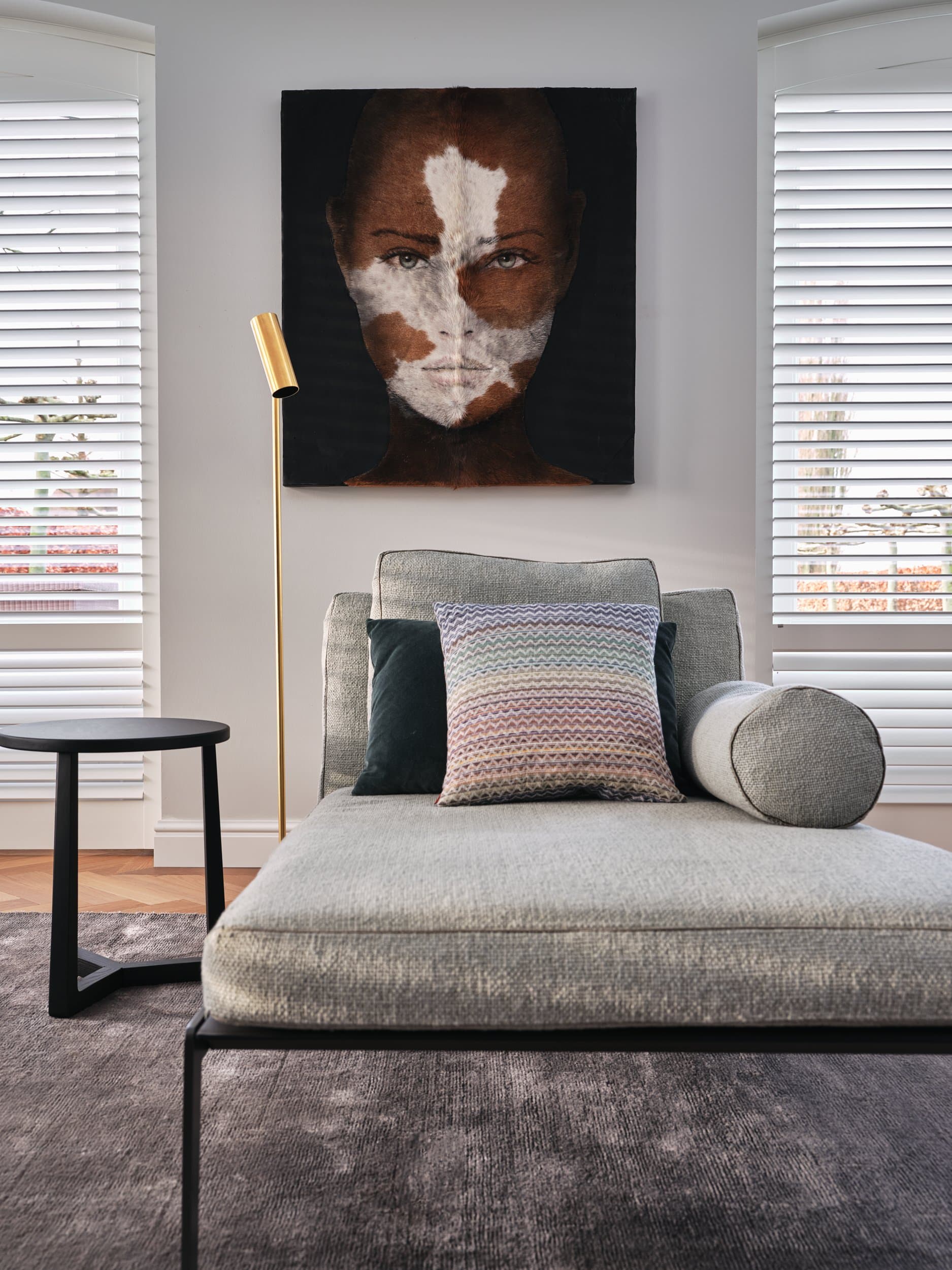 Slaapkamer met grijs linnen lounger, kleurrijke kussens en houten bijzettafel