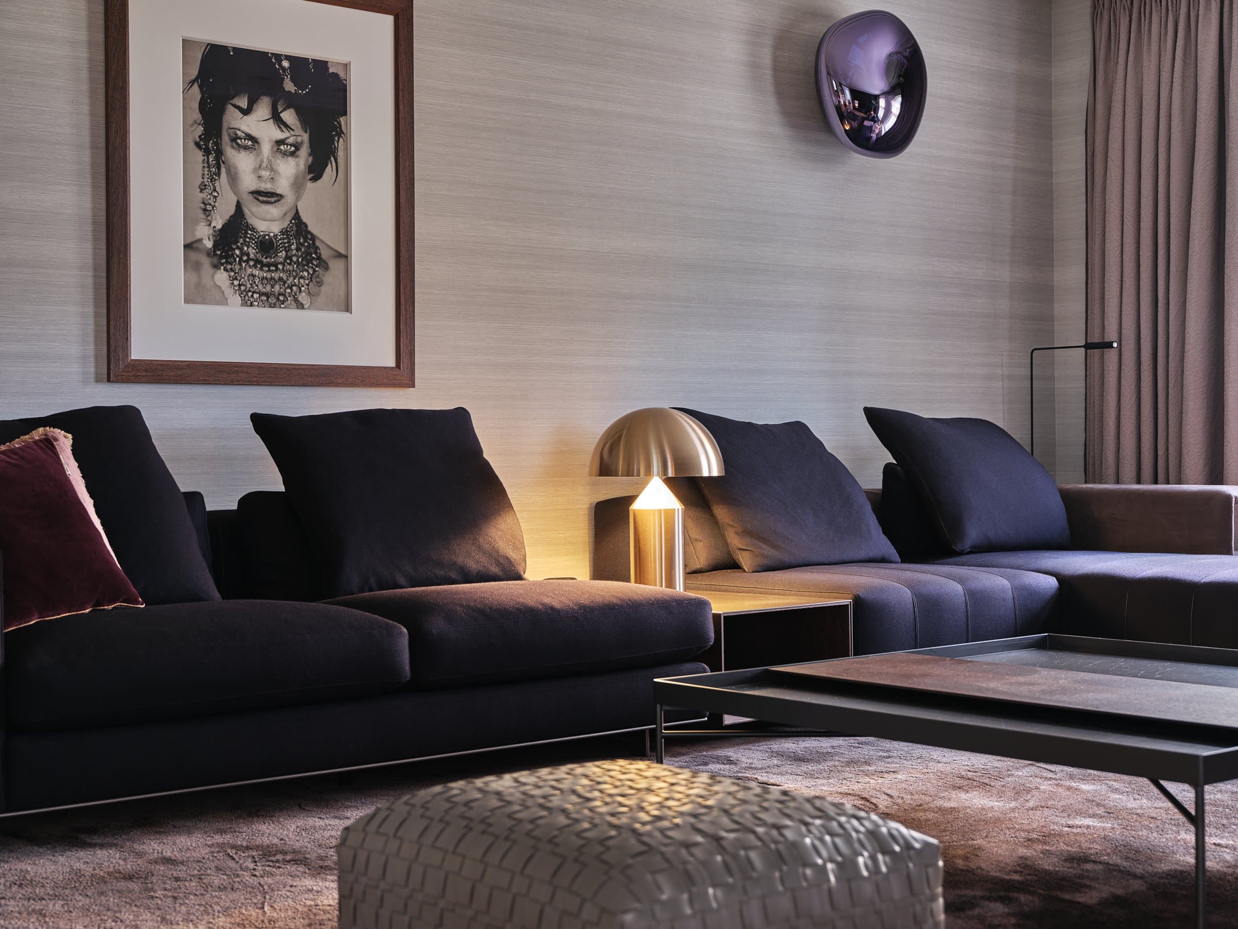 Zithoek met donkerblauwe modulaire bank, gouden tafellamp en abstracte kunstwerk
