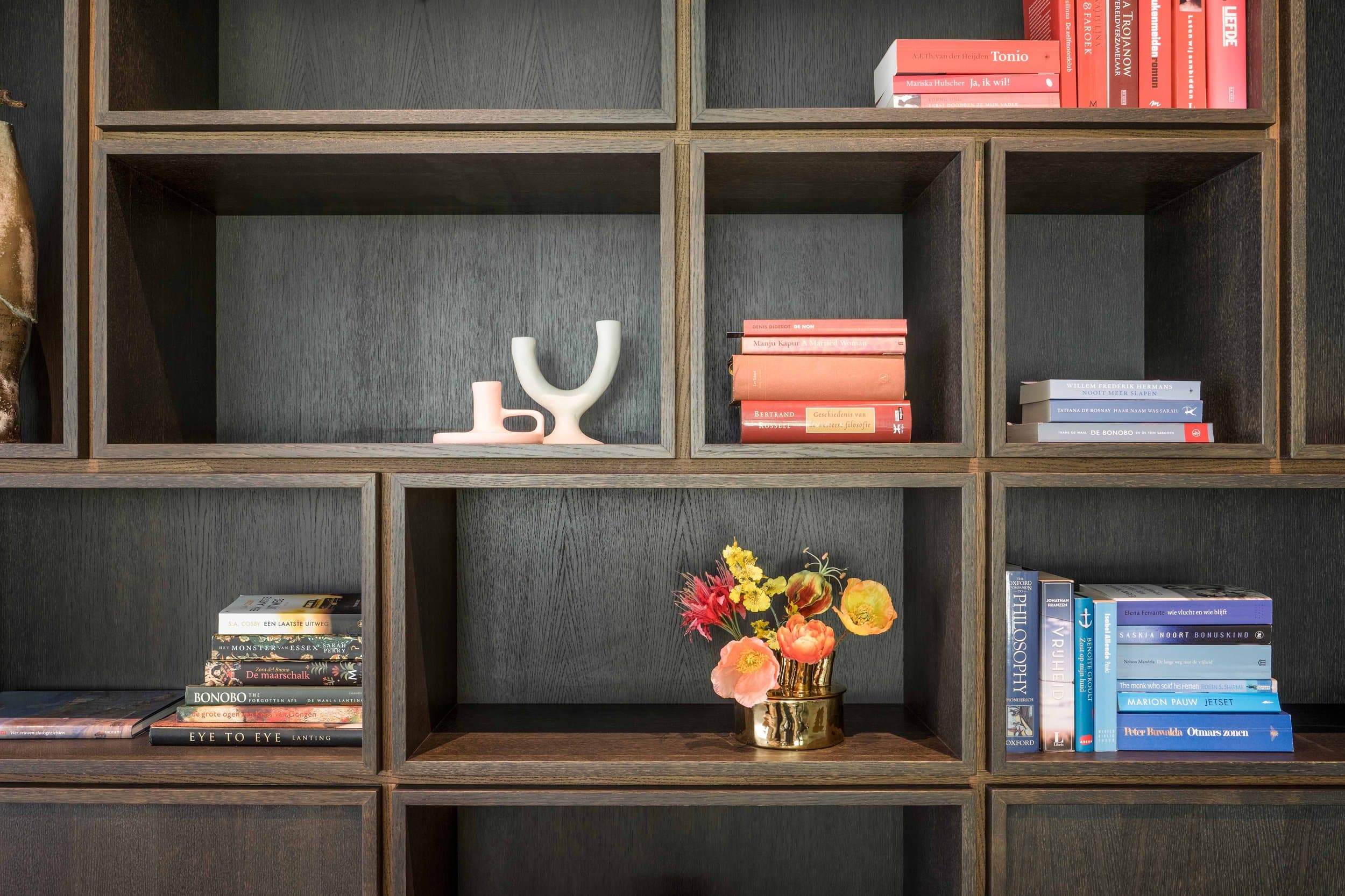 Boekenrek in donkergrijs hout met boeken, bloemen en decoratieve objecten