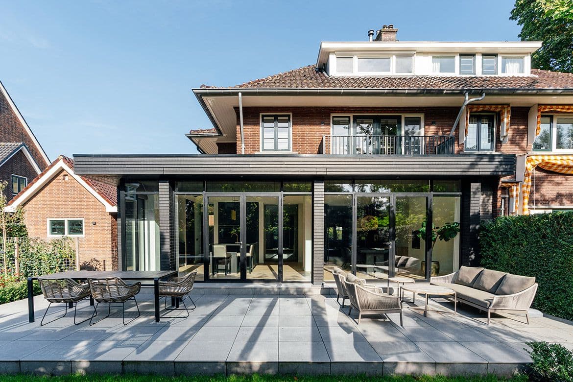Moderne uitbouw met zwarte aluminium frames en brede grijze terrassen