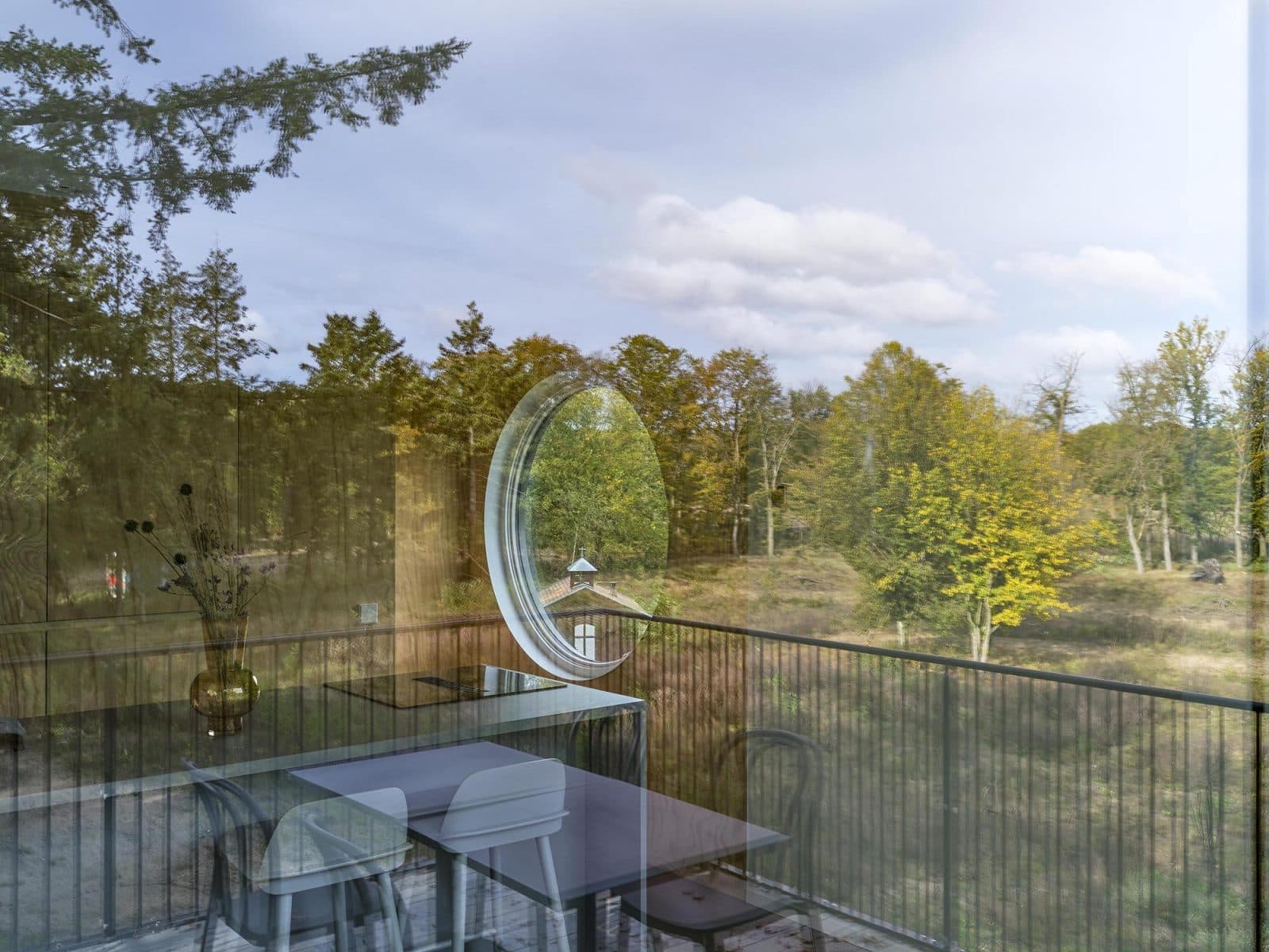 Glastuin met ronde spiegel en stalen railing over natuurlandschap