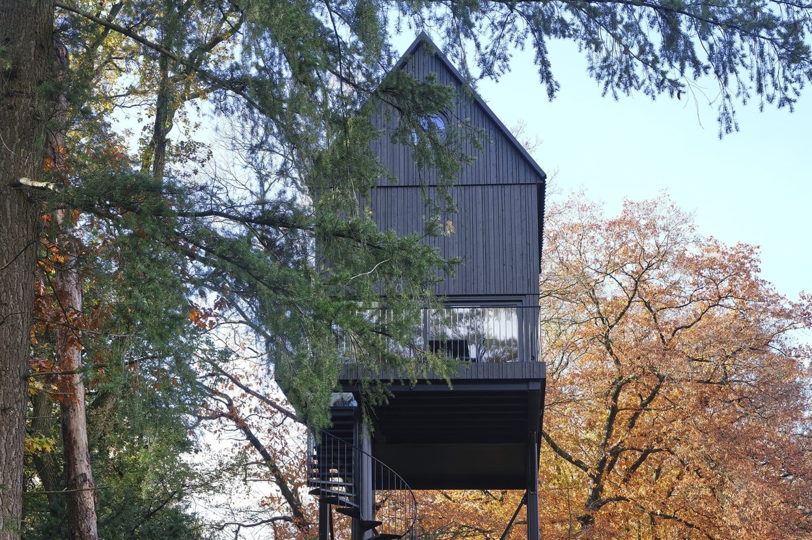 Zwart houten woonmodule op palen tussen herfstkleuren