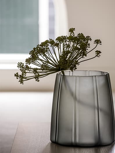 Detail grijze glazen vaas met groene tuinplant op houten vloer
