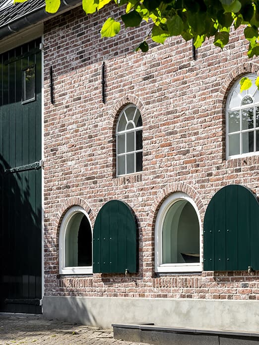 Voorgevel bakstenen boerderij met groene luiken en gewelfde ramen