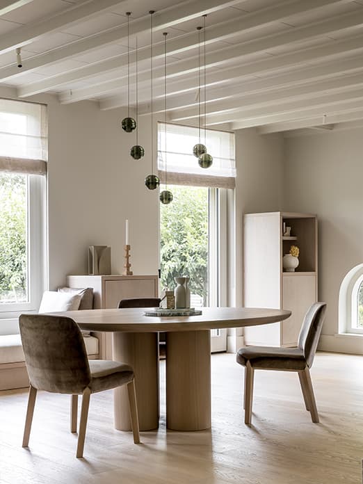 Eetkamer ronde houten tafel hangende donkere lampen houten kasten