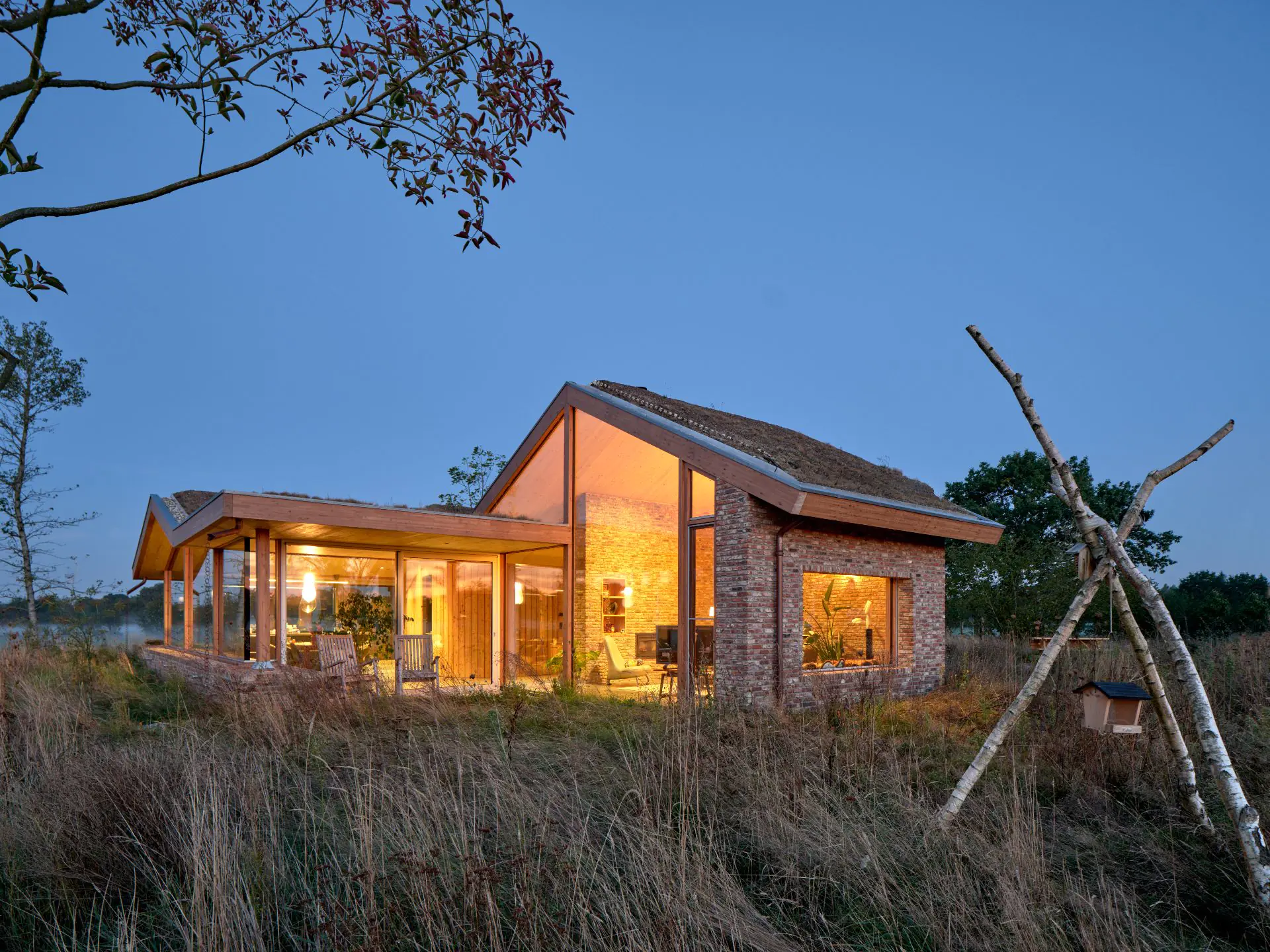 Verlichte villa met houten vormen in mistig landschap bij zonsondergang