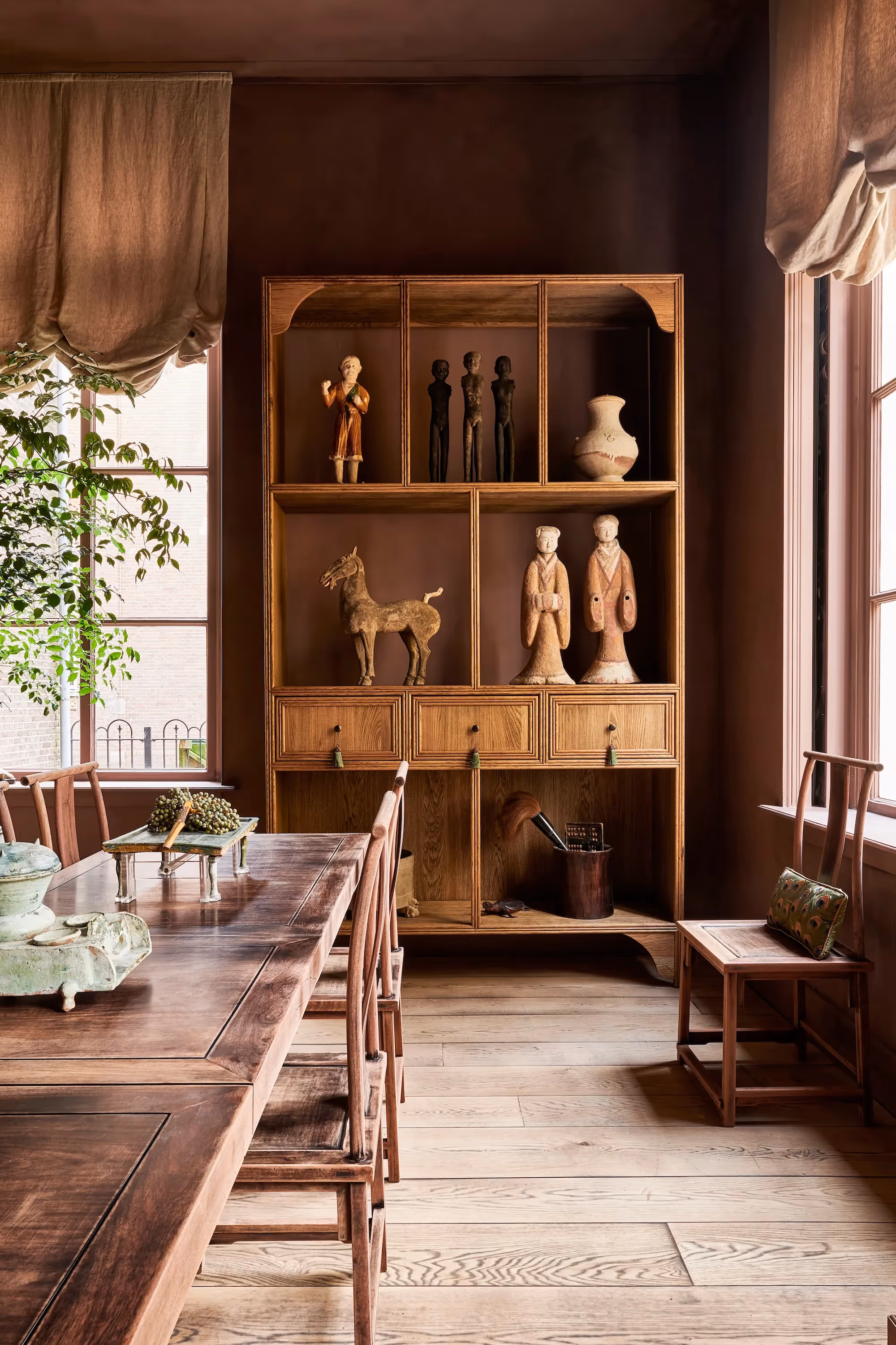Eetkamer met houten vitrinekast, sculpturen en rood-bruine muren