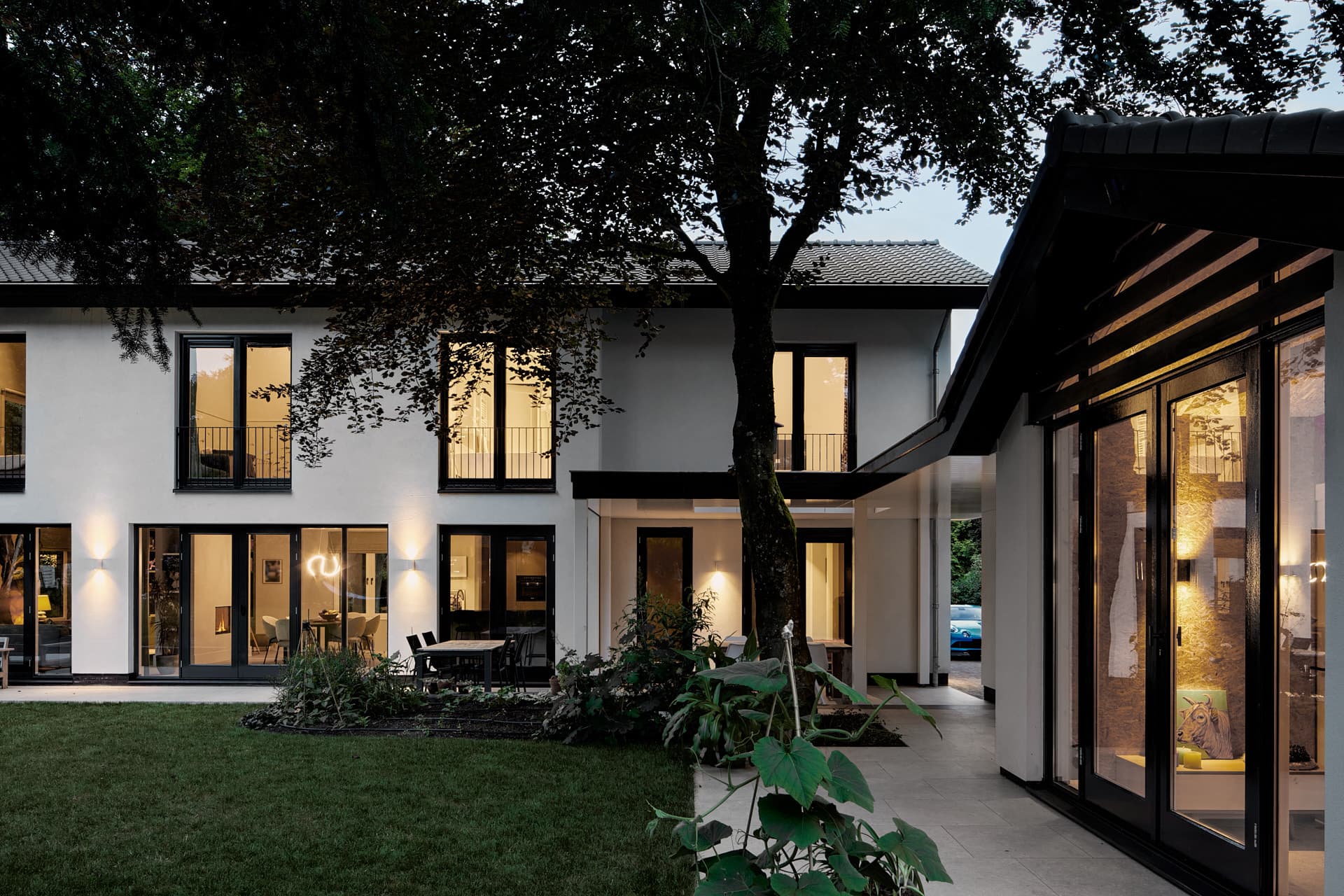 Moderne witte villa met grote ramen, terras en oude boom in tuin