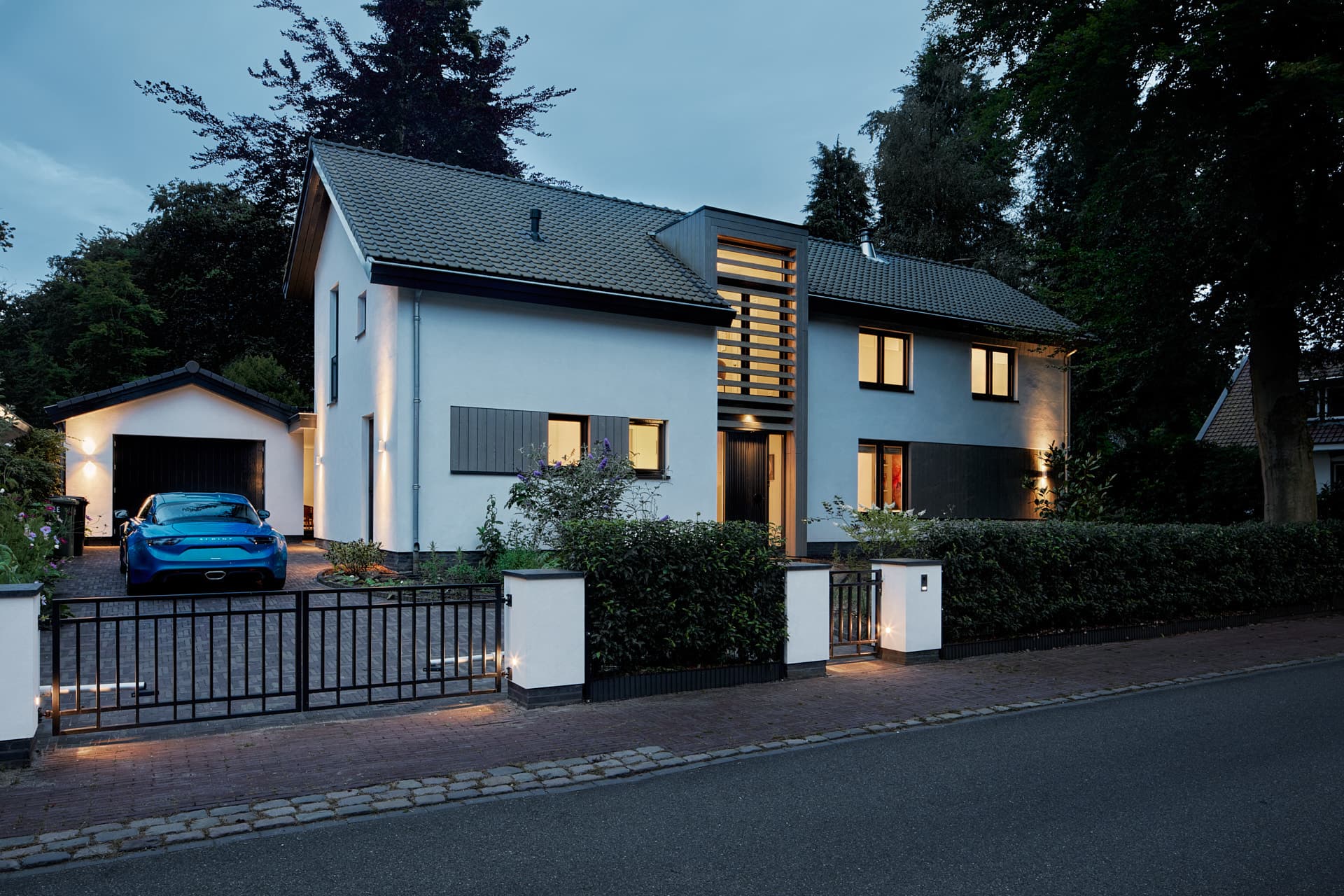 Moderne villa met garage, metalen hek en blauw voertuig zichtbaar