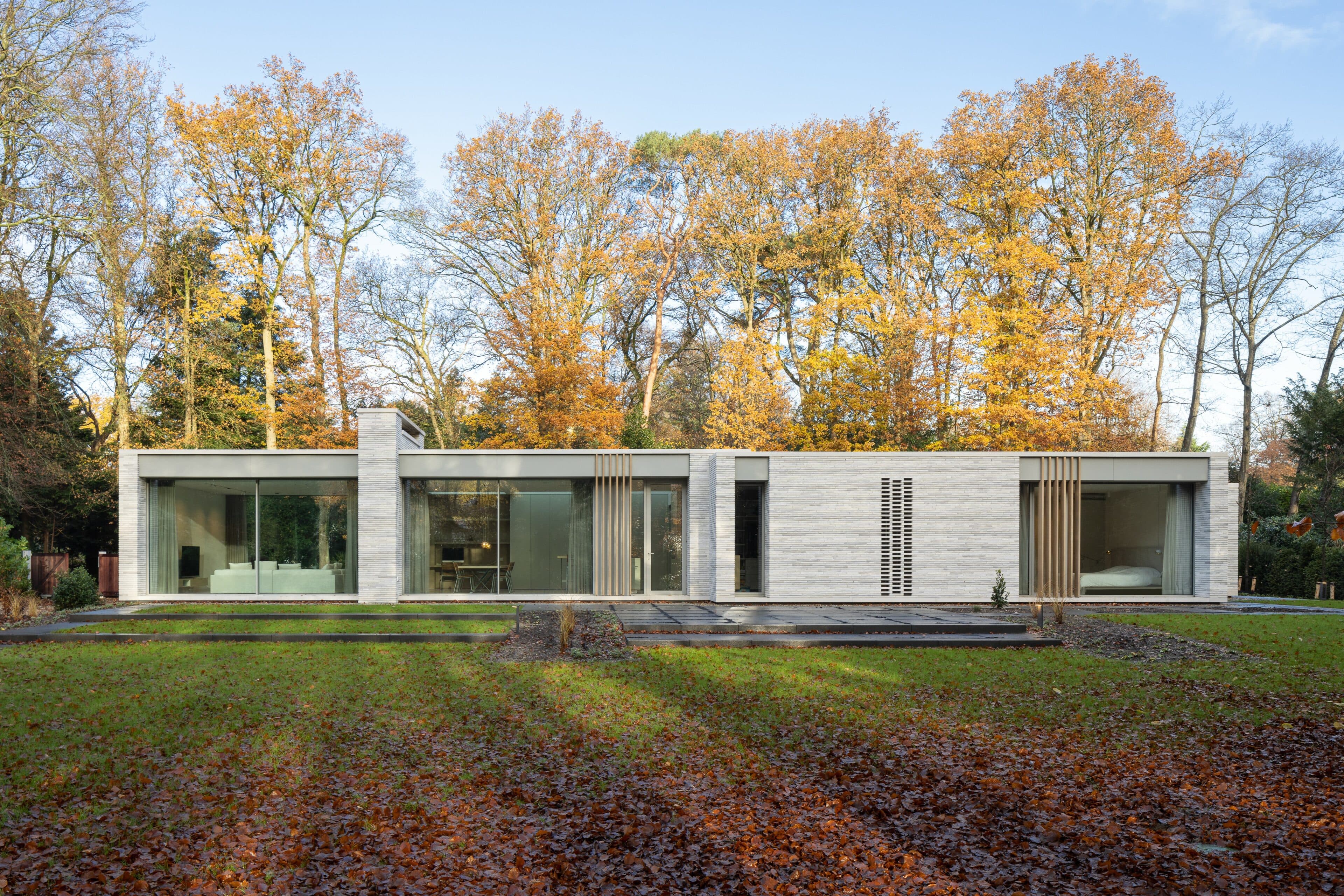 Moderne villa met witte baksteengevel en grote raampartijen in herfstlandschap
