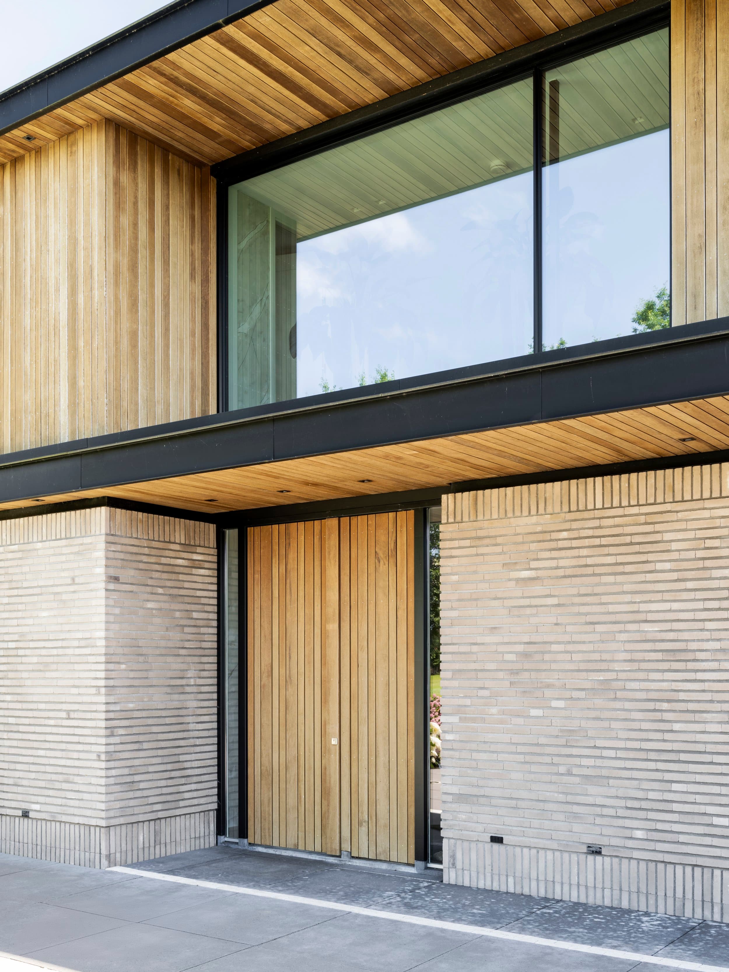 Ingang met houten verticale schuifdeuren en zwart raamkozijn