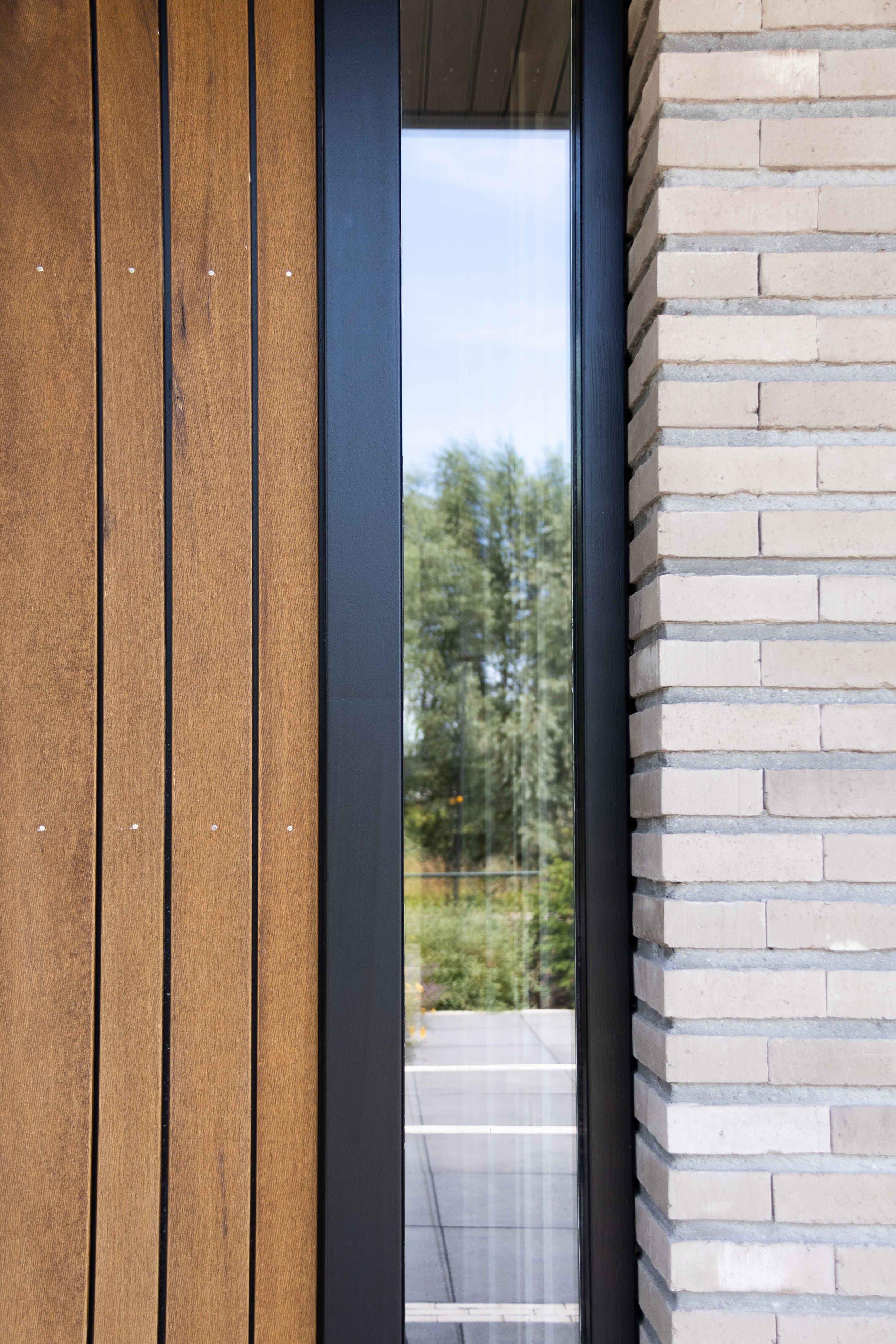 Detail groot raamkozijn met donker frame en boslandschap zicht