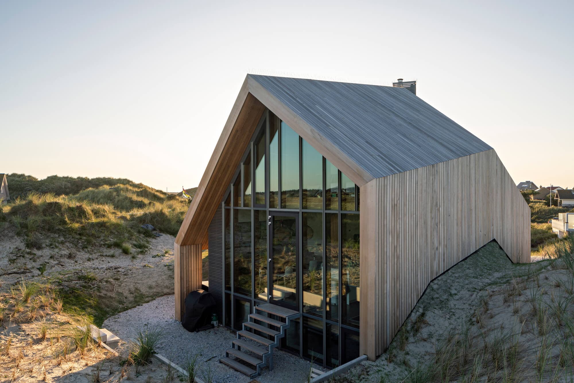 Moderne strandhuisje met houten gevel en grote glazen voorgevel op duinen