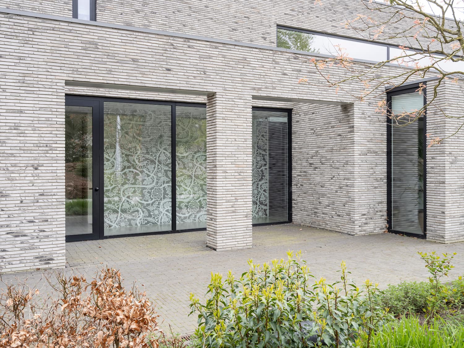 Moderne bakstenen villa met grote glazen ramen en groene tuin