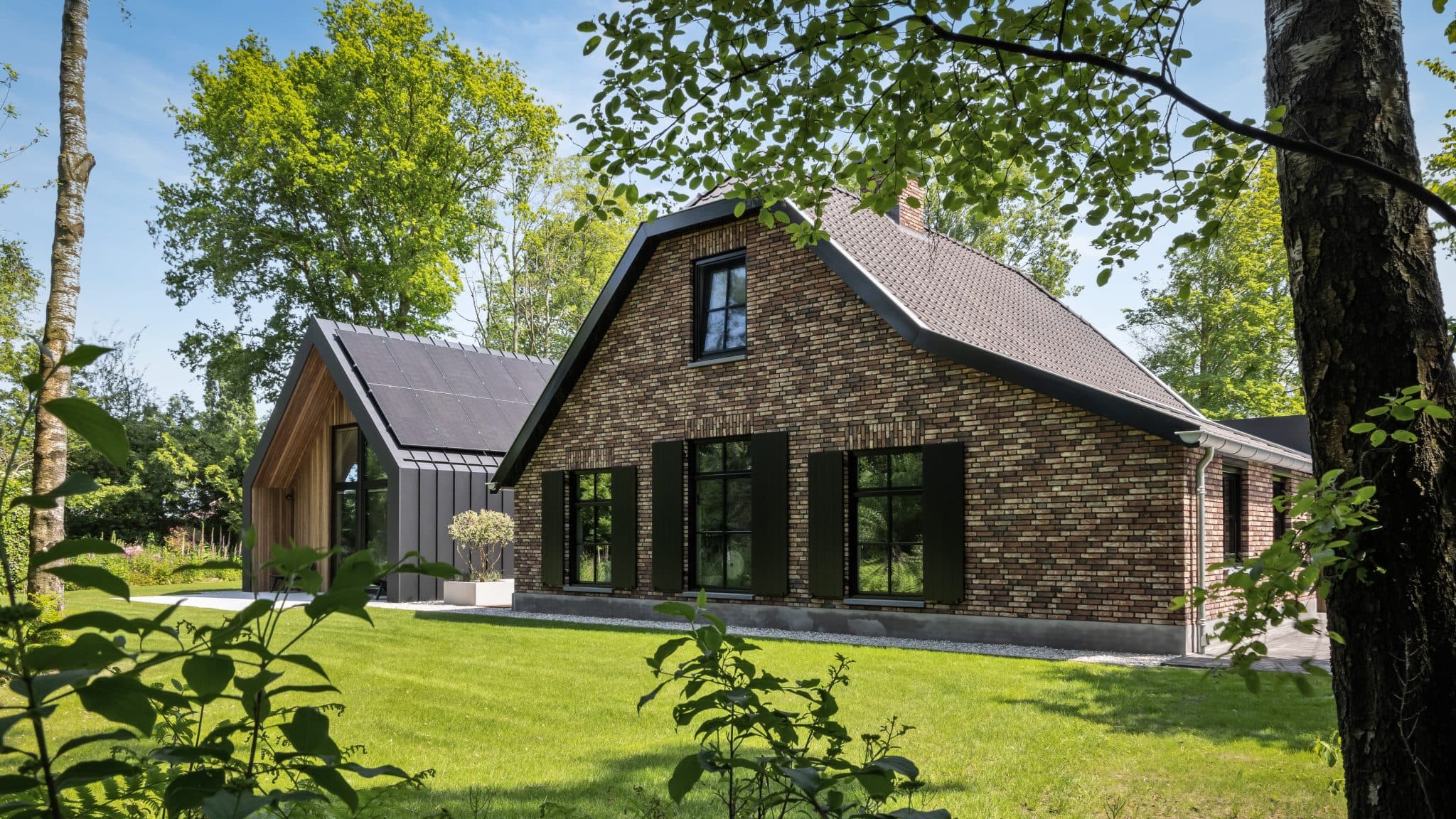 Bakstenen villa met zwarte raamkozijnen, houten aanbouw en groen gazon