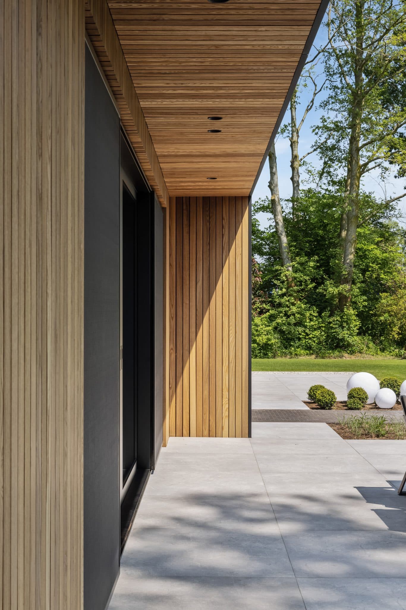 Overdekte doorgang met verticale houten lamellen en grijze betonvloer