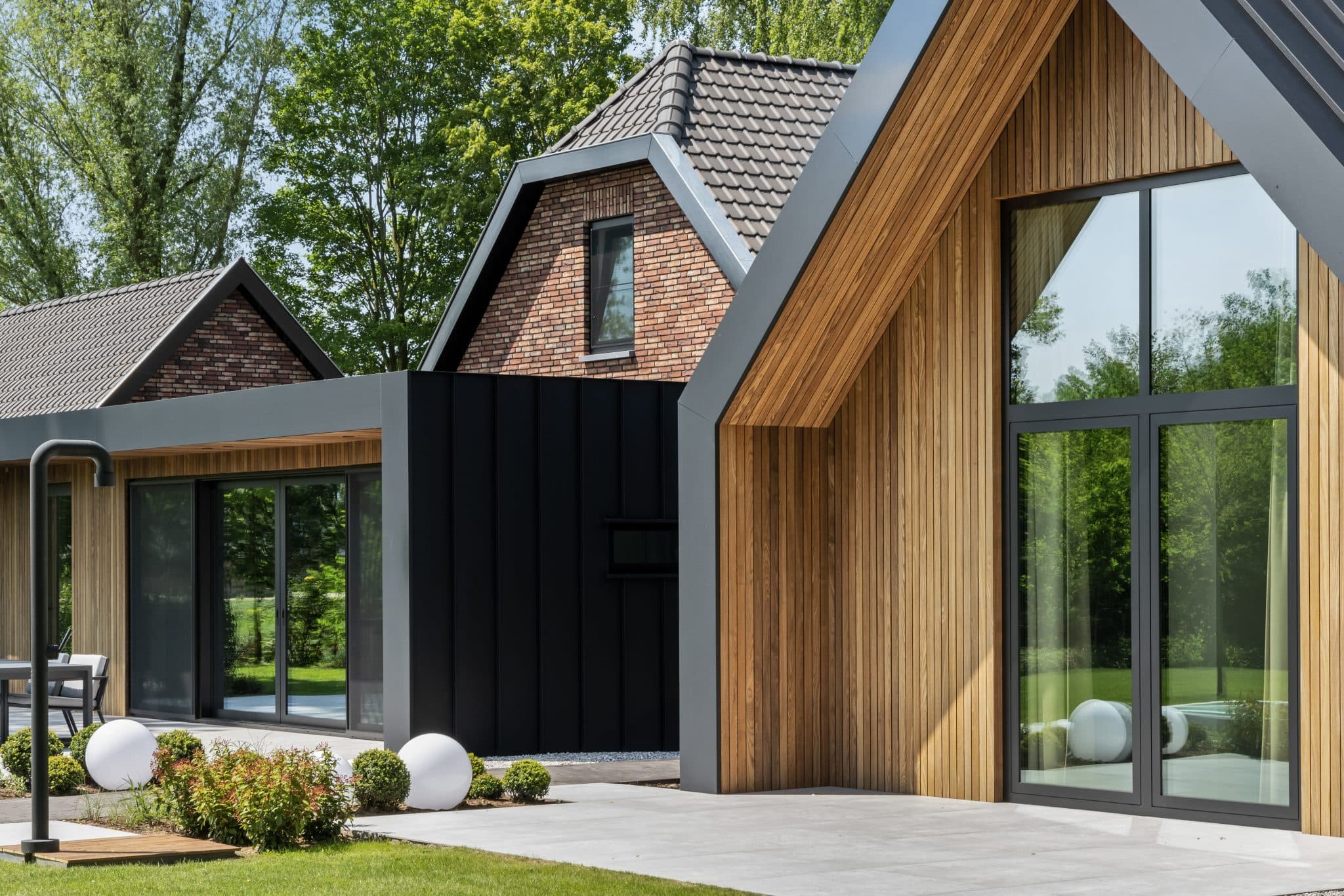 Moderne zwarte aanbouw met houten zijgevel en grijze betonnen oprit