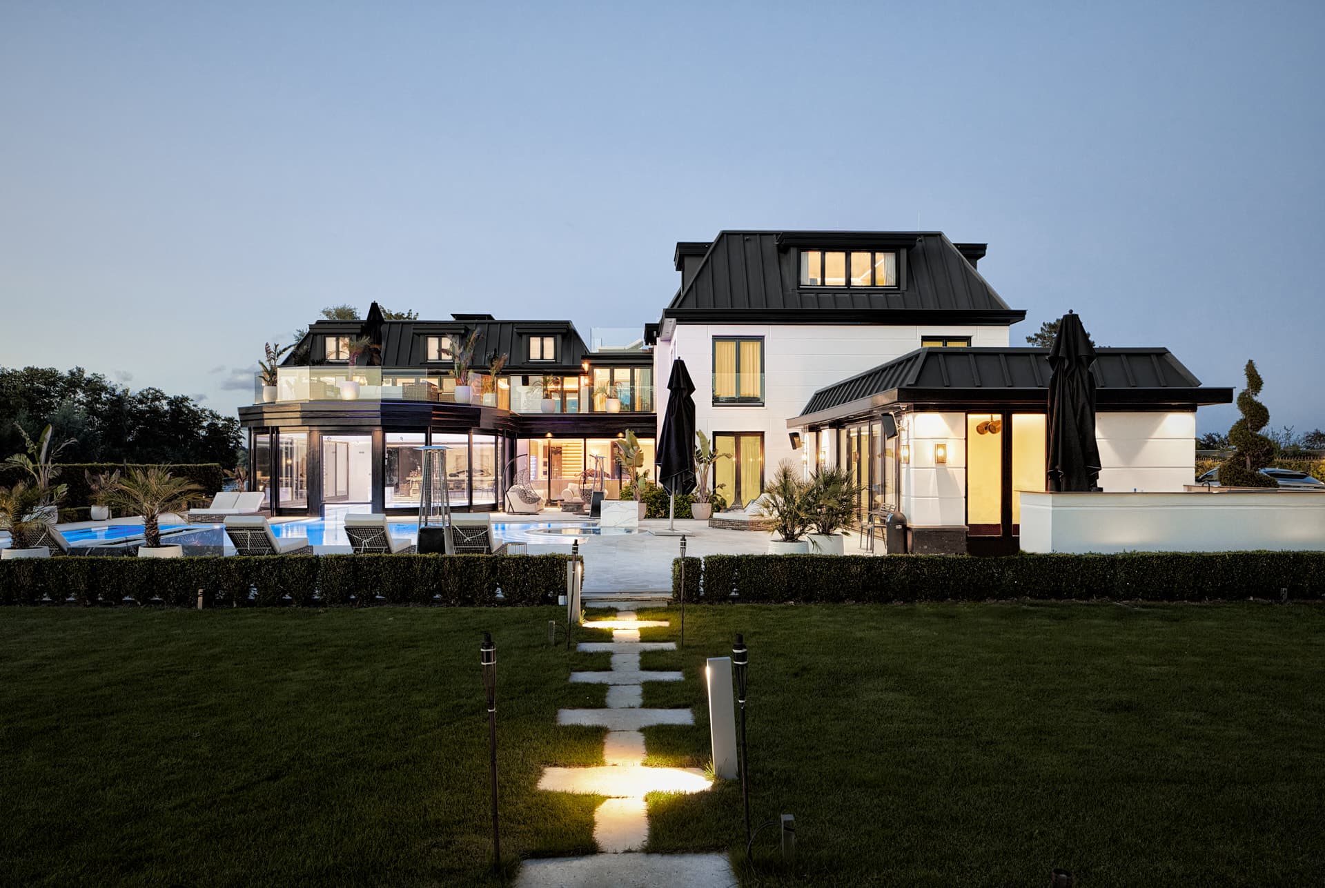 Moderne villa met zwarte daken, witte gevel en verlichte vijver in avondlicht