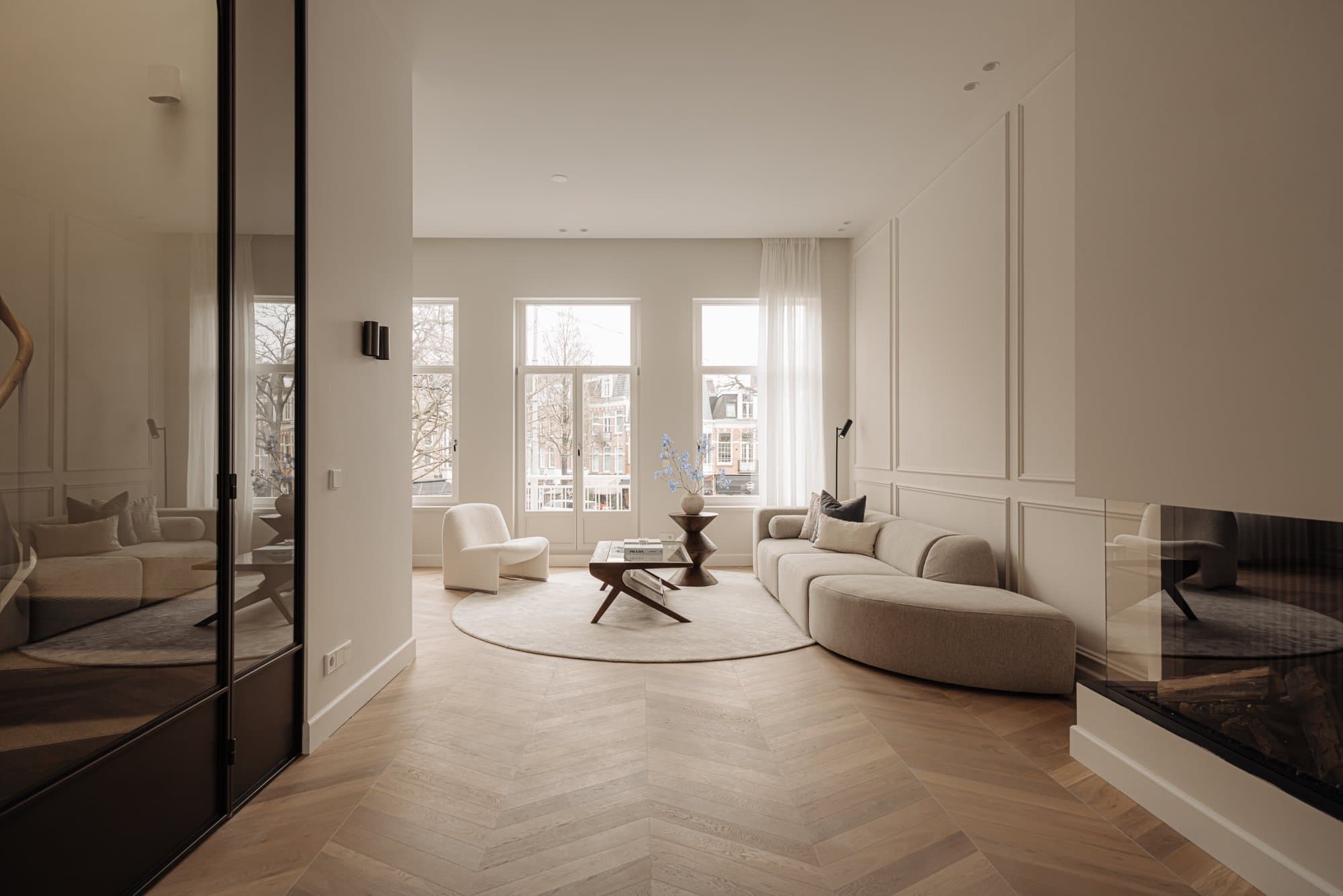 Woonkamer met grote ramen, beige meubels en houten vloer