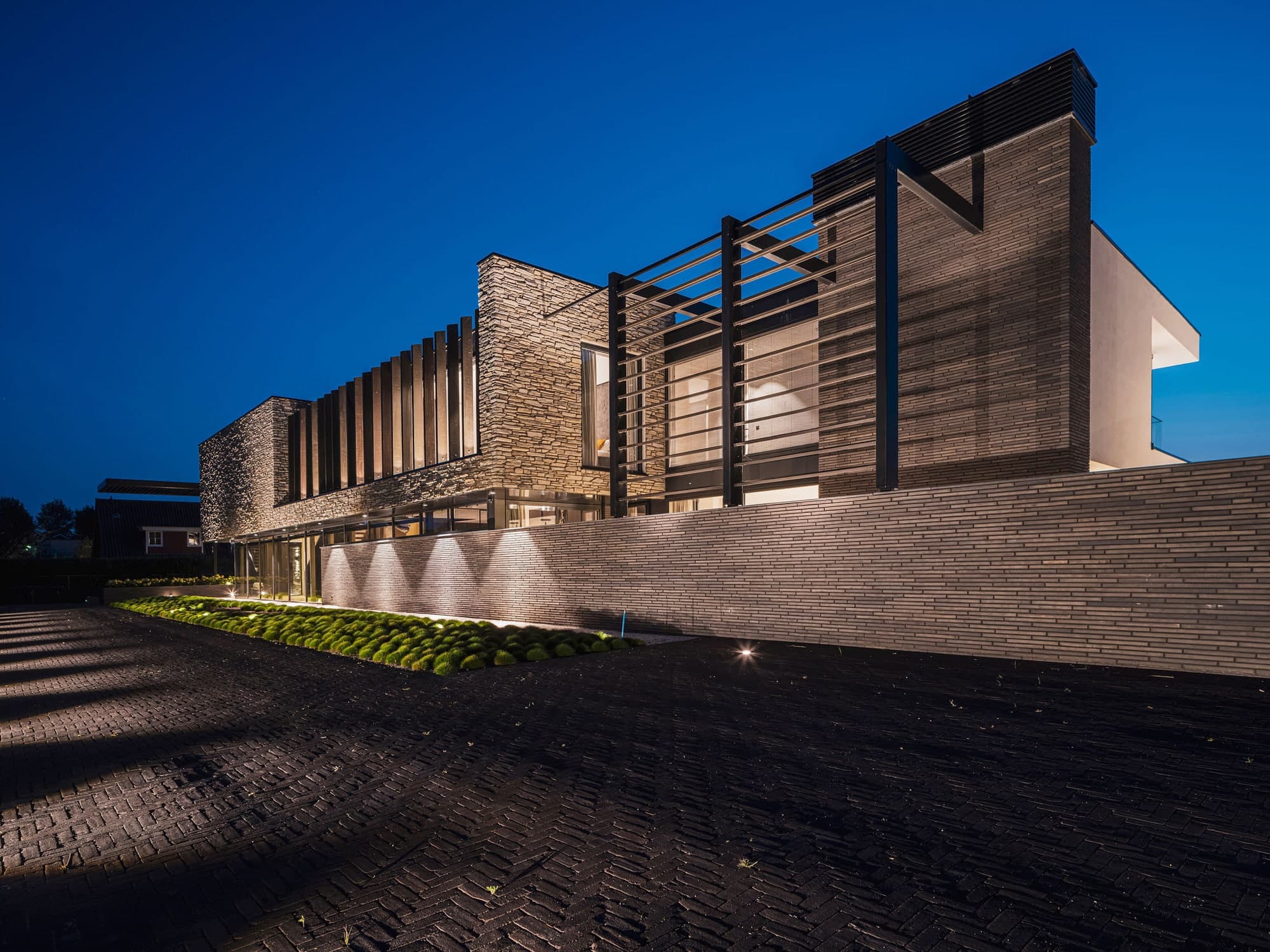Gevel met bakstenen en houten lamellen, verlichte sokkel en moderne carport