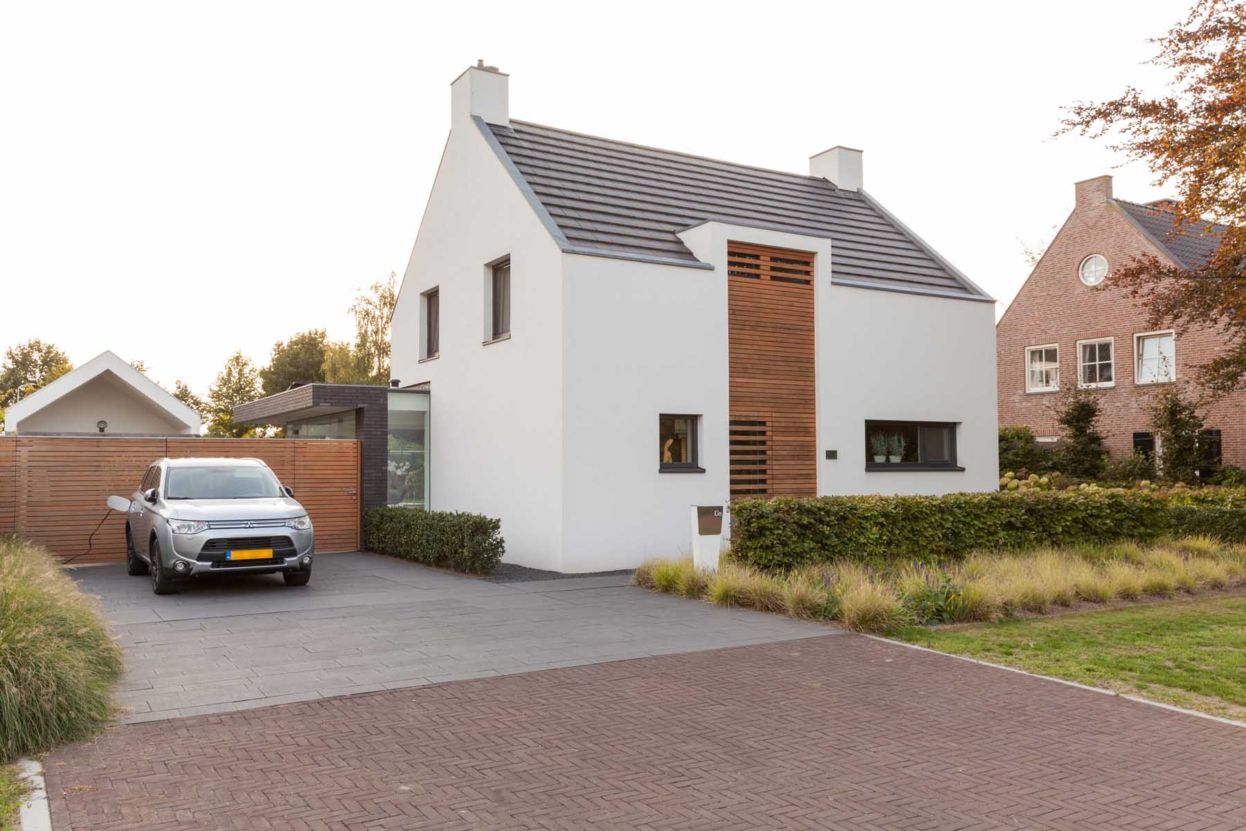 Witte moderne villa met houten accenten, carport en bakstenen buurwoning