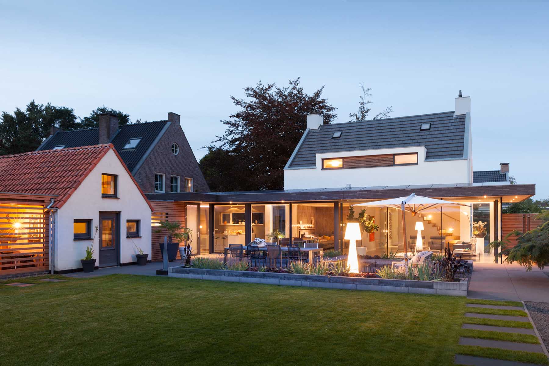 Moderne uitbouw met grote glazen schuifpuien, terras en verlichte voorgevel