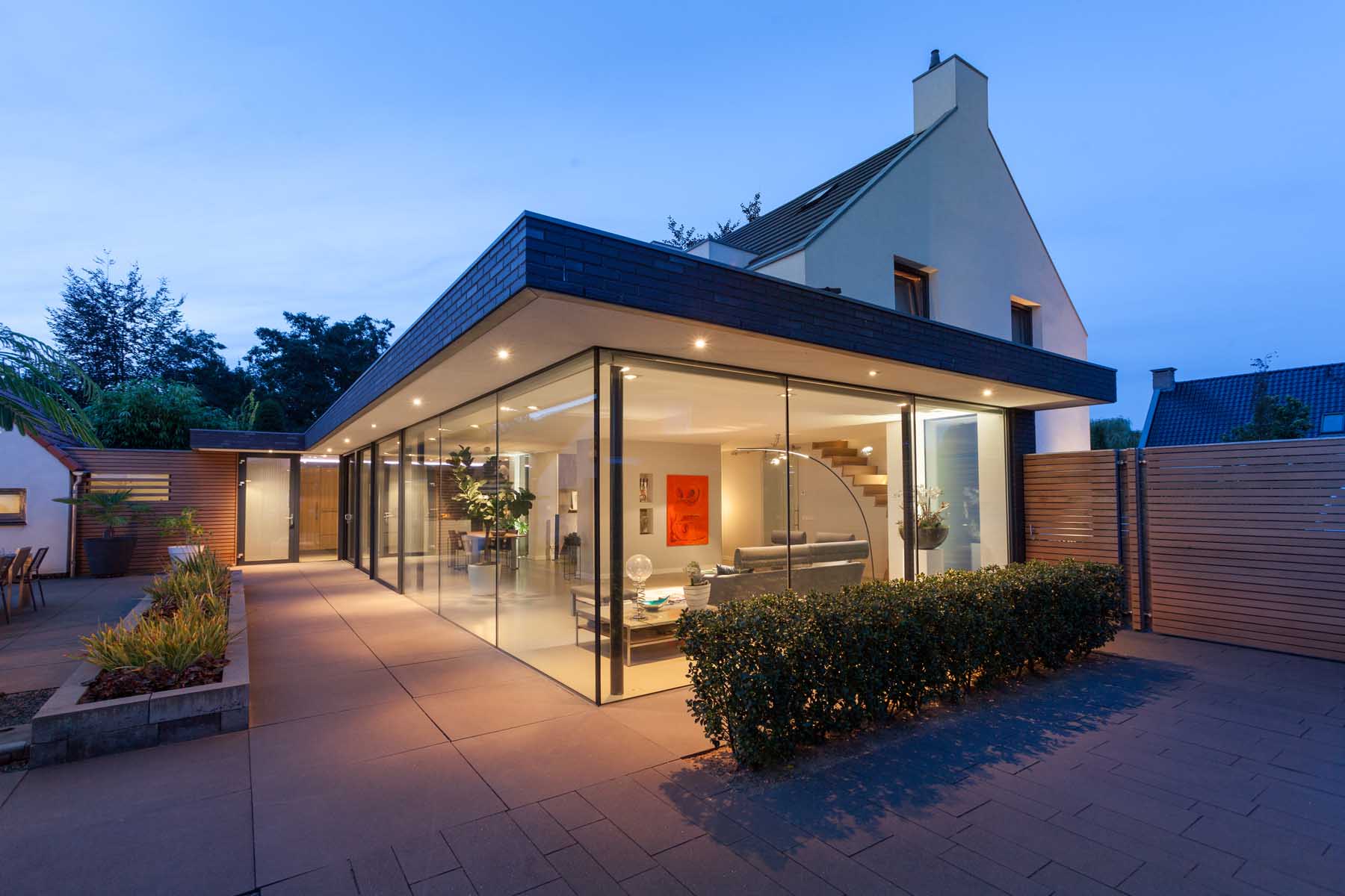 Moderne villa met rieten dak, glazen uitbouw en verharde terras bij schemering