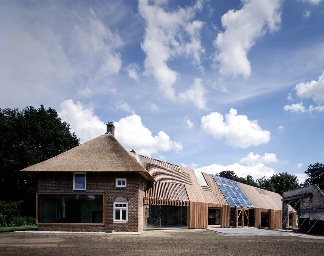 Traditionele boerderij met rietgedak en moderne houten aanbouw met zonnepanelen