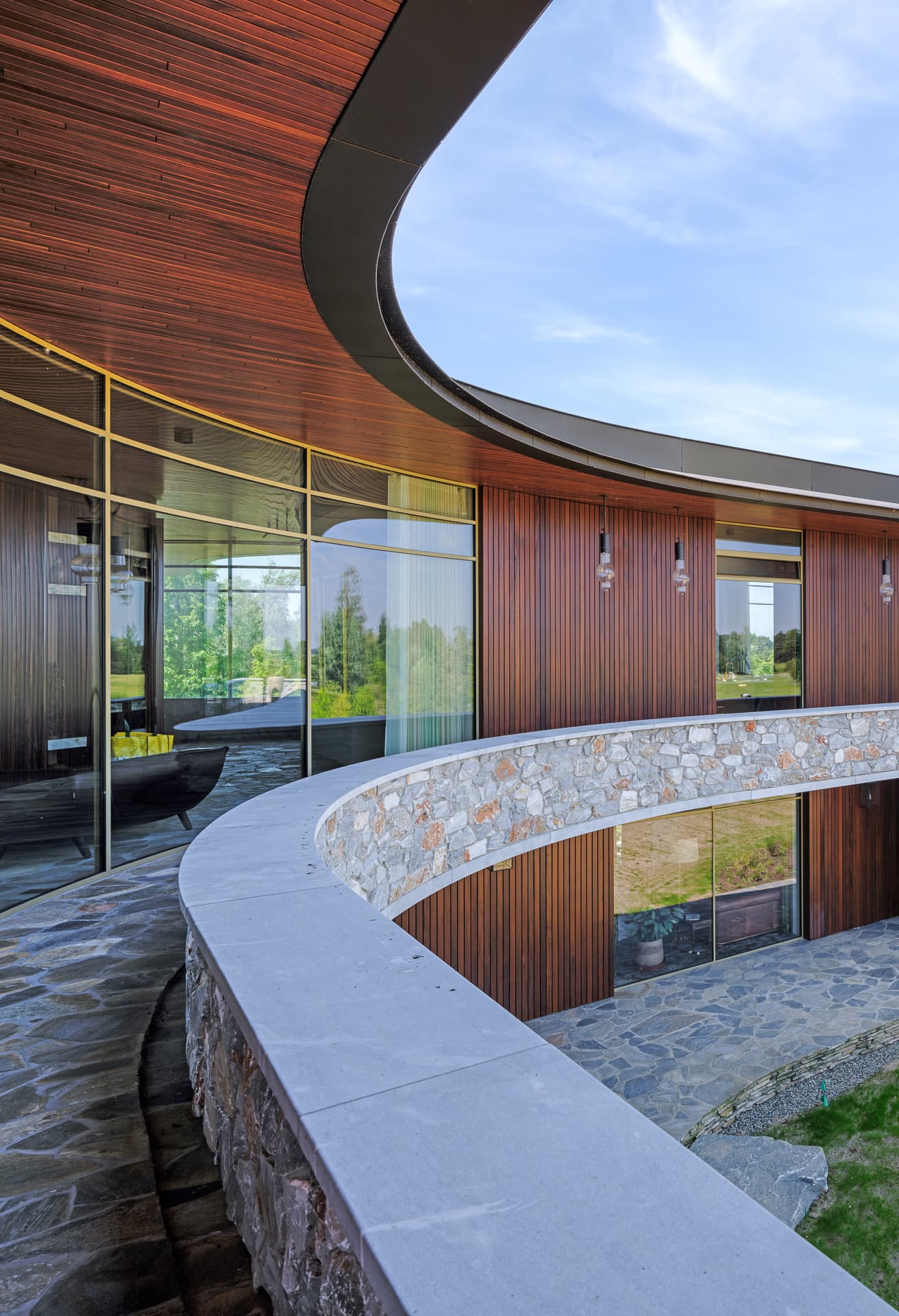 Curved stenen muur en houten gevelbekleding met glazen elementen
