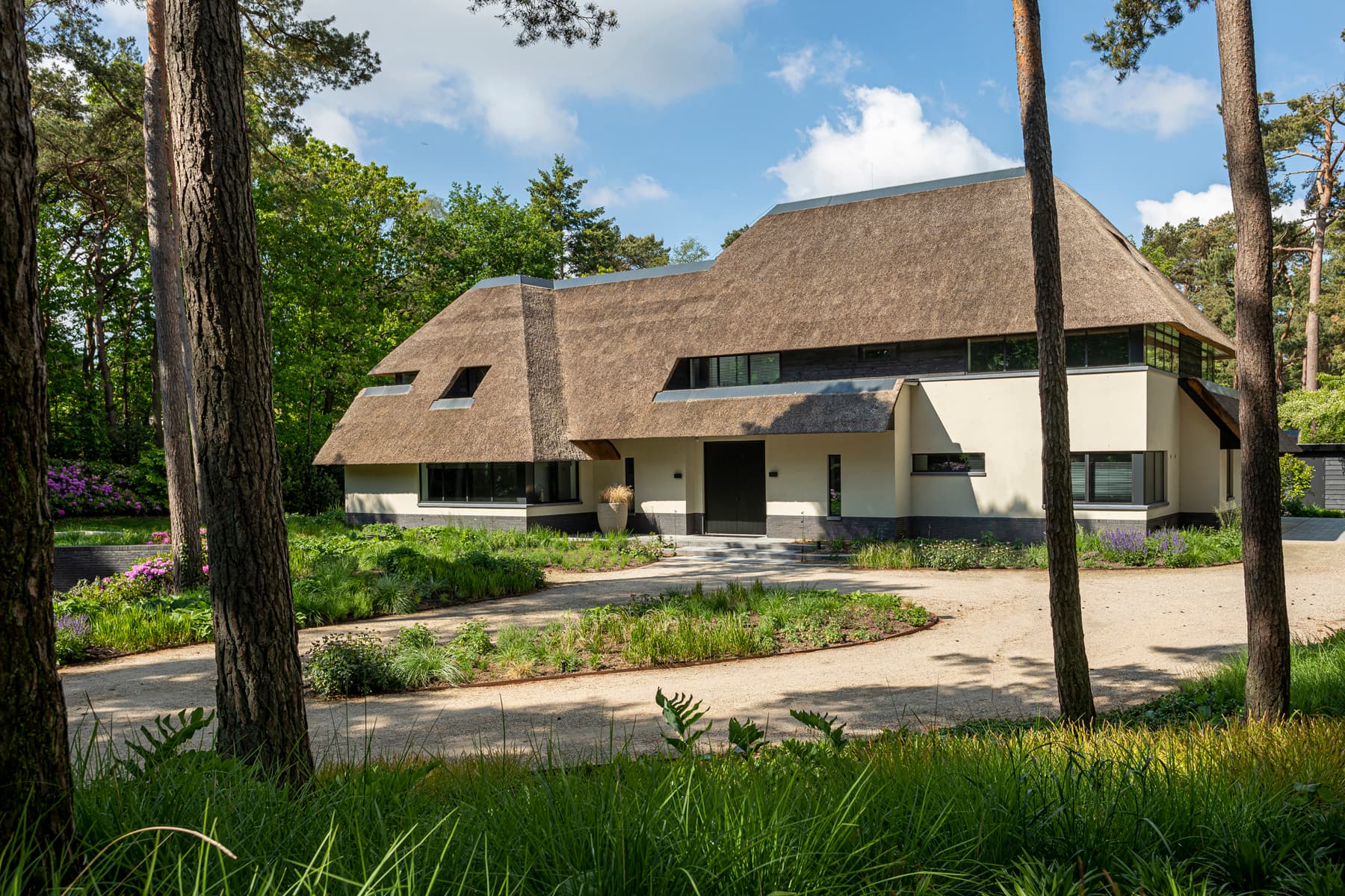 Voorgevel villa met rieten dak, witte pleisterkant en donkere raamlijsten