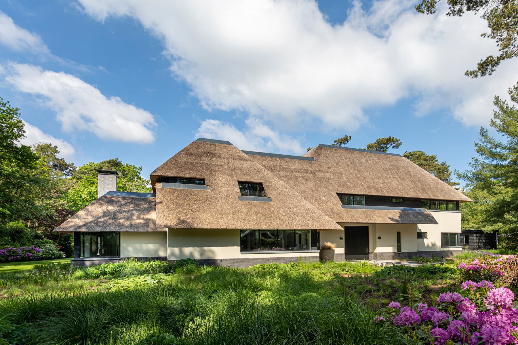 Zijgevel villa met rieten dak, paarse rhododendrons en grasveld