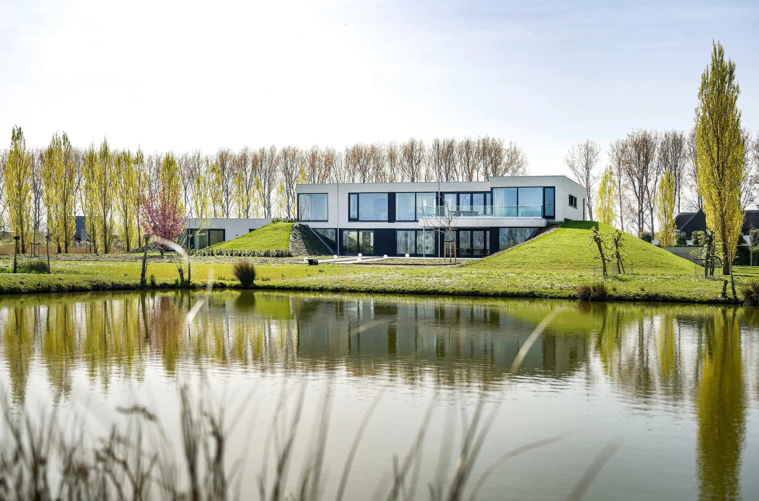 Moderne woning met zwarte baksteen, grote ramen en groene aarden wallen aan water