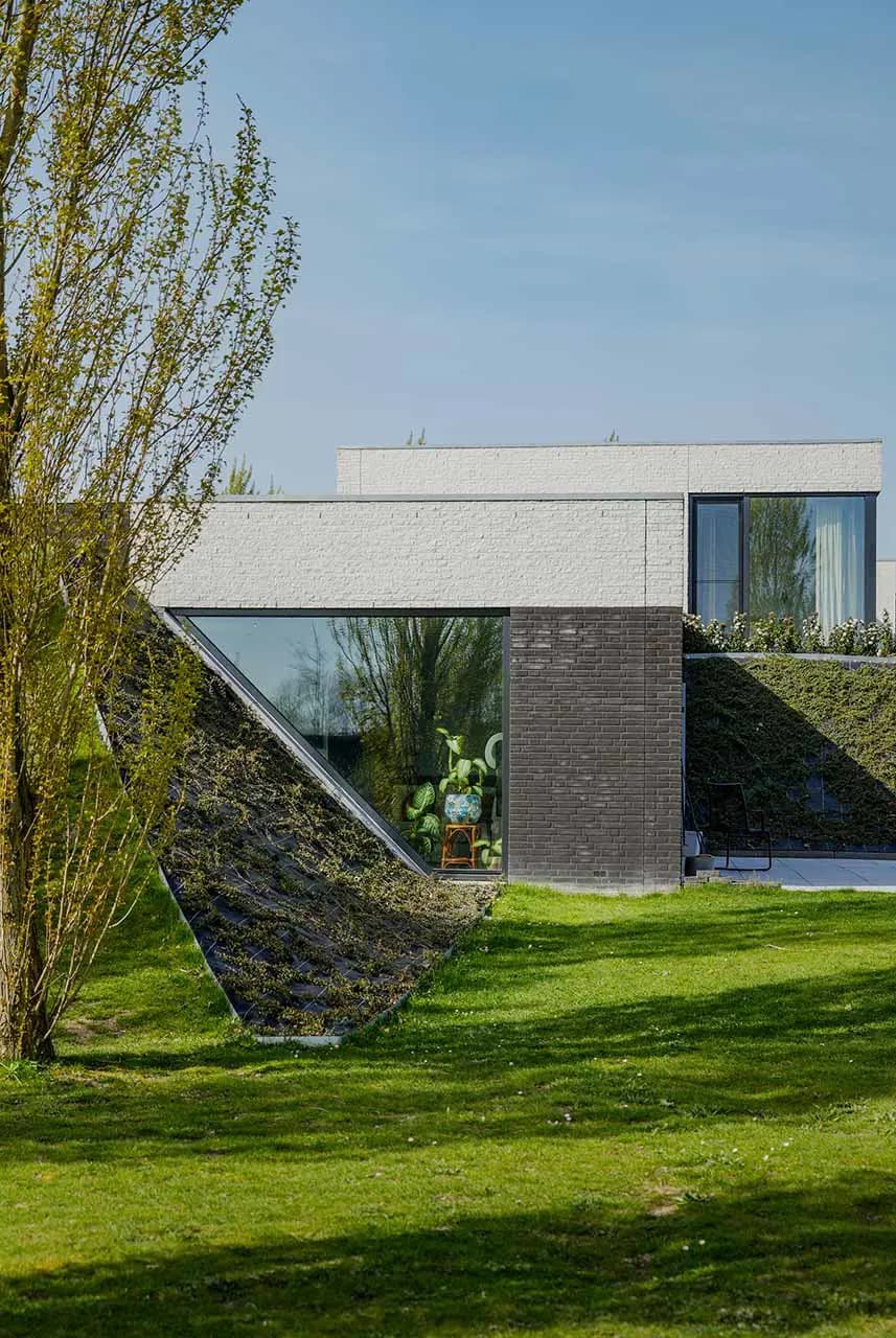 Moderne woning met groene aarden wallen, bakstenen gevel en diepe terraszone