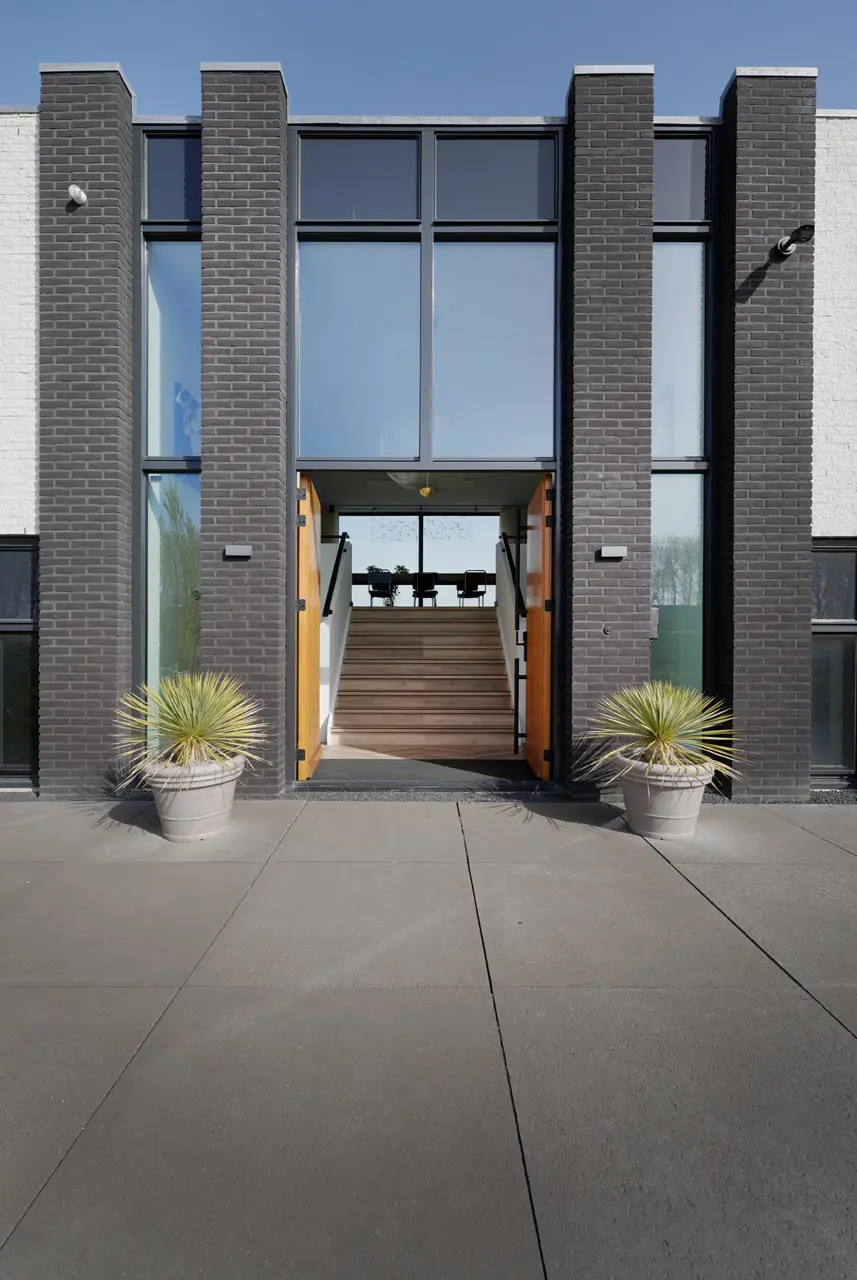 Ingangsportaal met grijze bakstenen pilasters, gele houten deur en grote beglazing