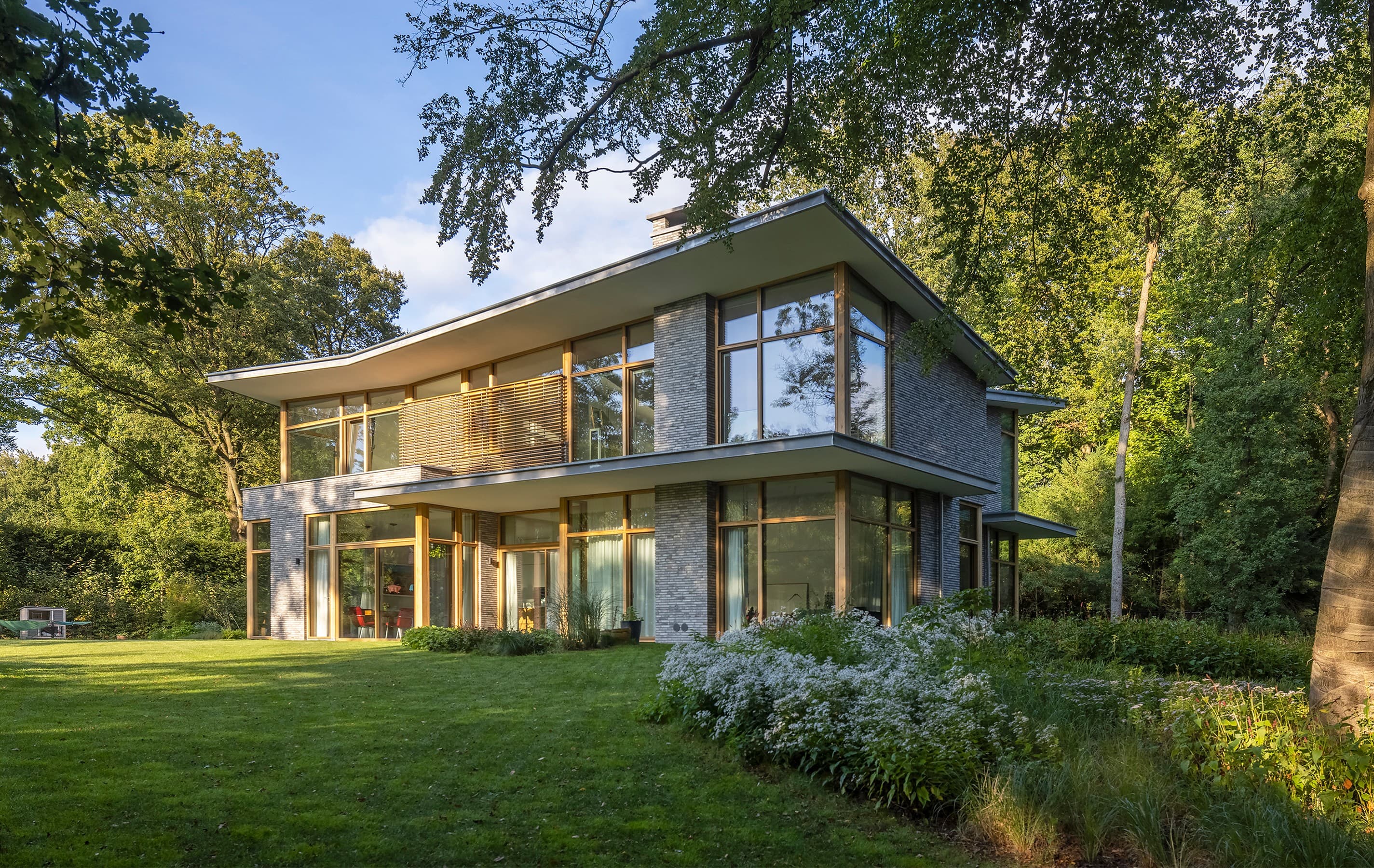 Moderne twee-verdiepingswoning met grote glazen ramen en groene tuin