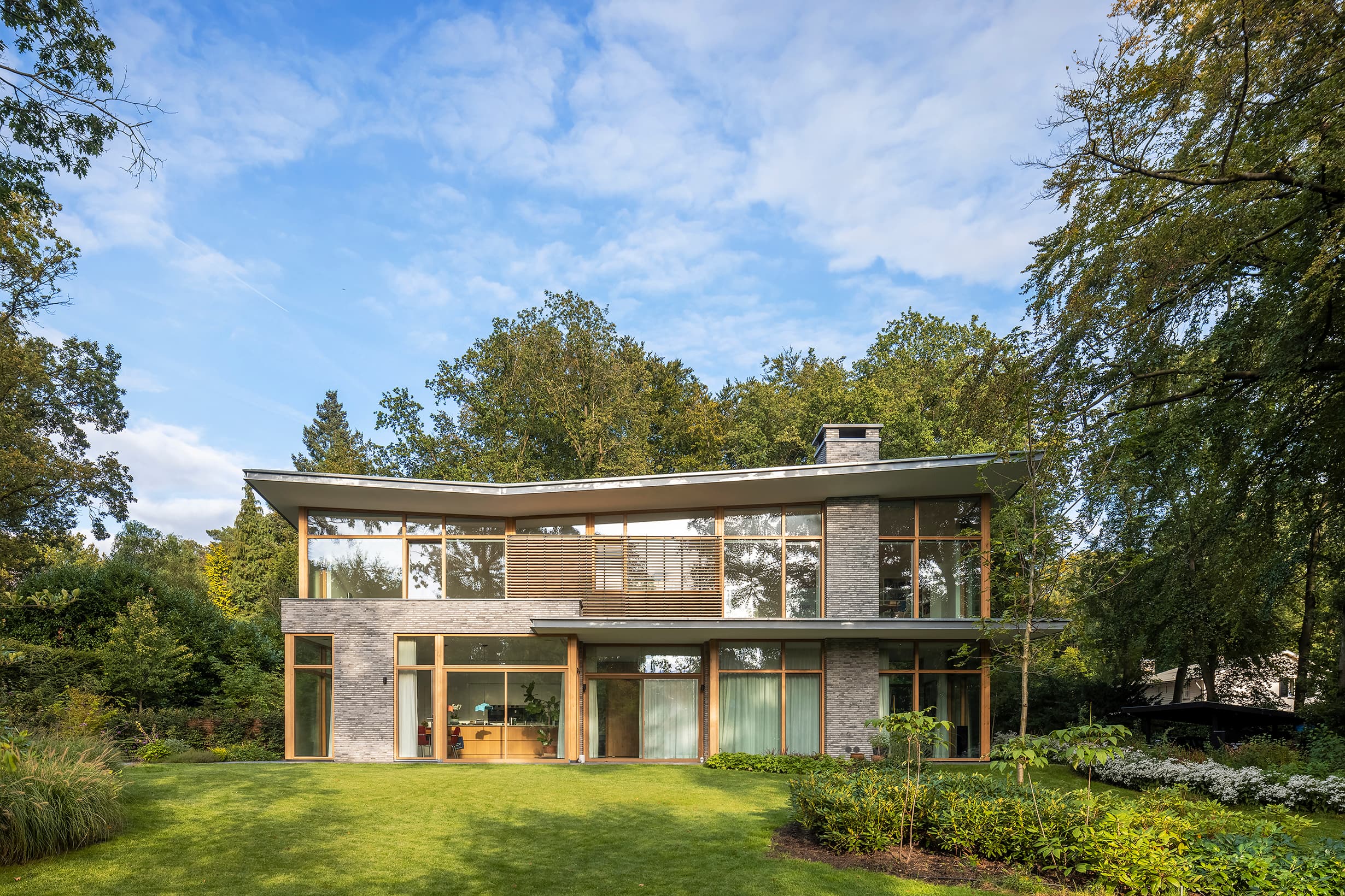Moderne twee-laagse woning met baksteenmuur, houten omlijsting en groene achtertuin
