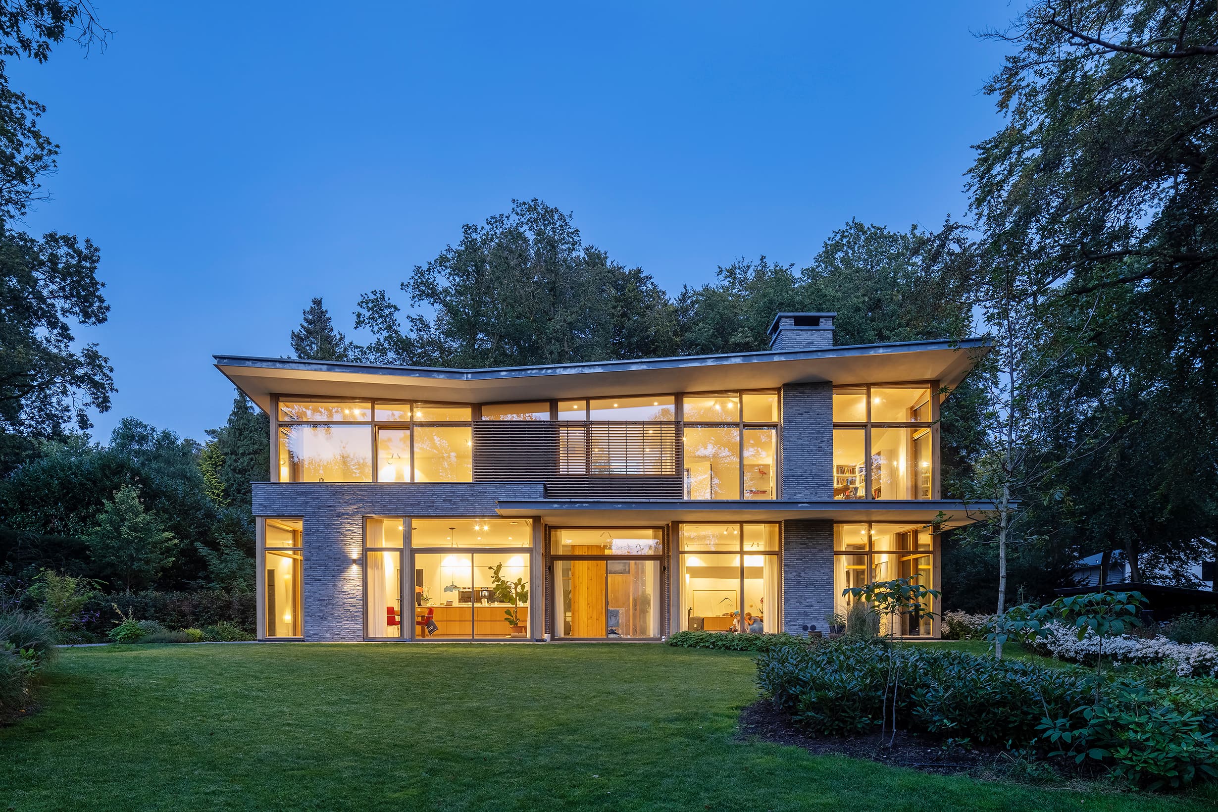 Verlichte moderne villa met baksteengevel en grote glazen puien 's avonds