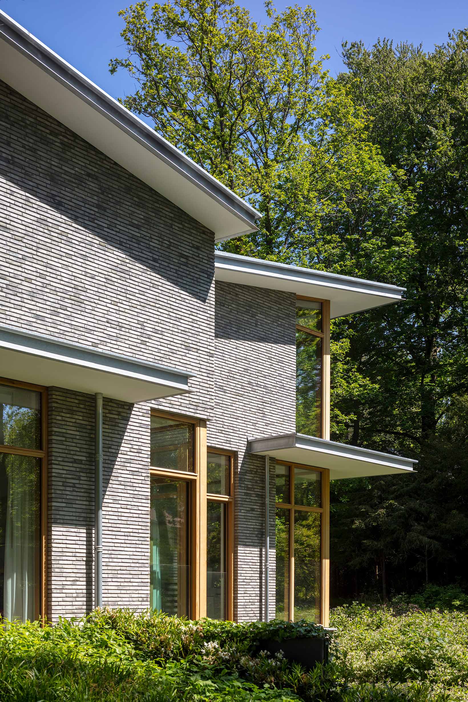Geveldetail met bakstenen, houten kozijnen en overstek op groene achtergrond
