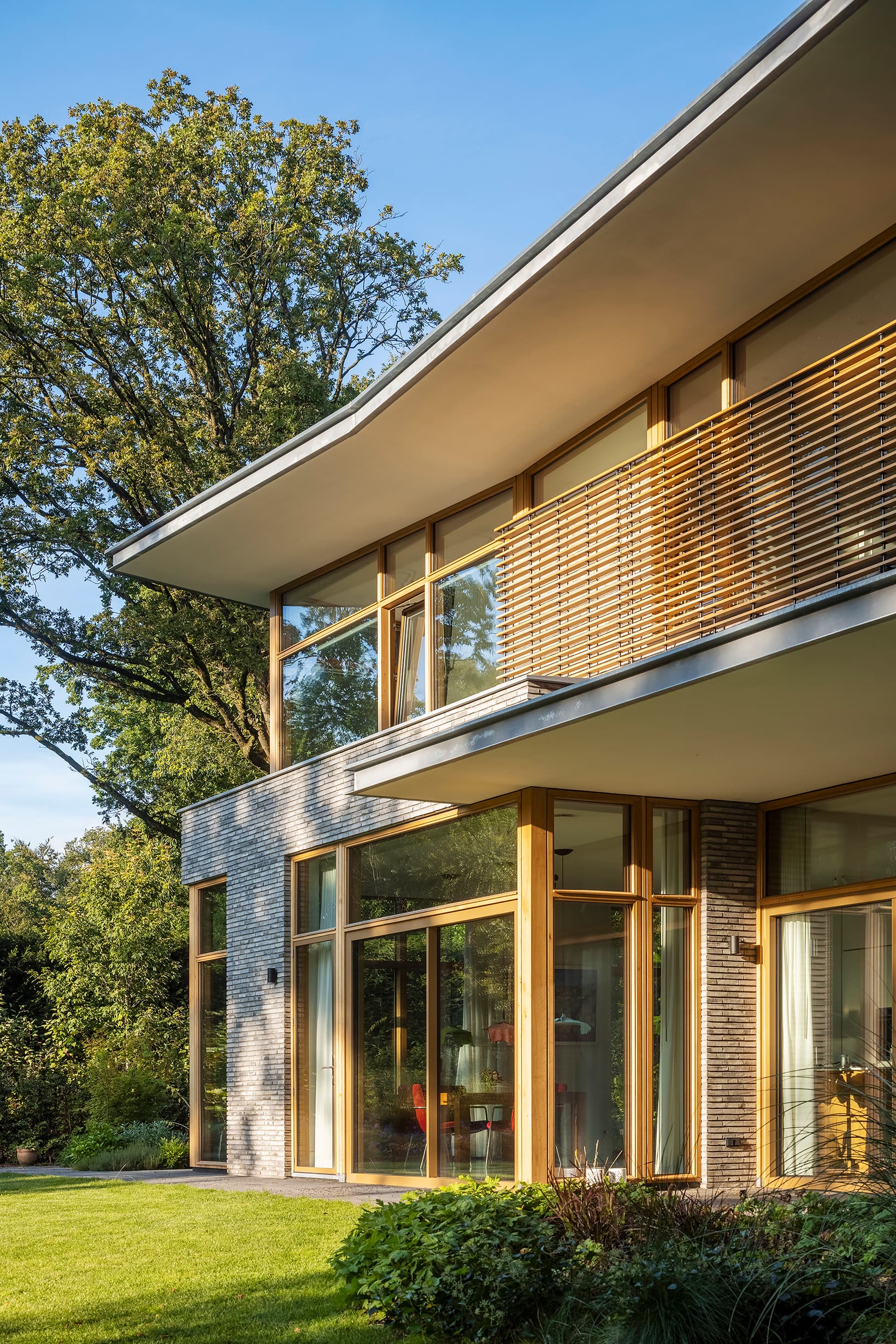 Woonhuisdetail met baksteengevel, houten lamellen en grote glazen schuifdeuren