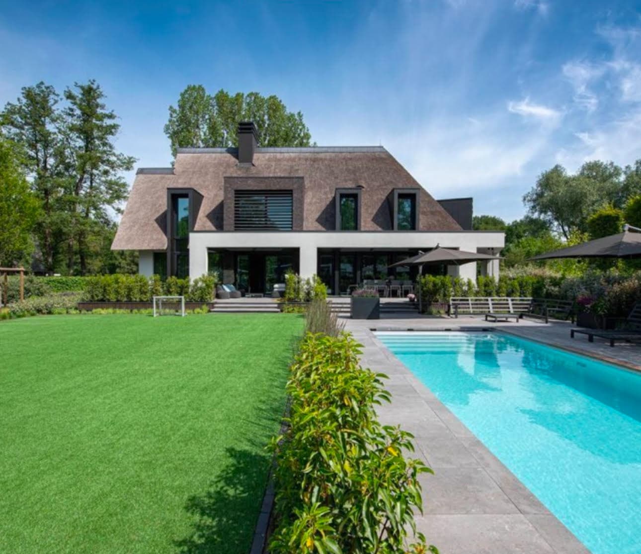 Zwembad met houten terras, riet-gedekte villa op achtergrond