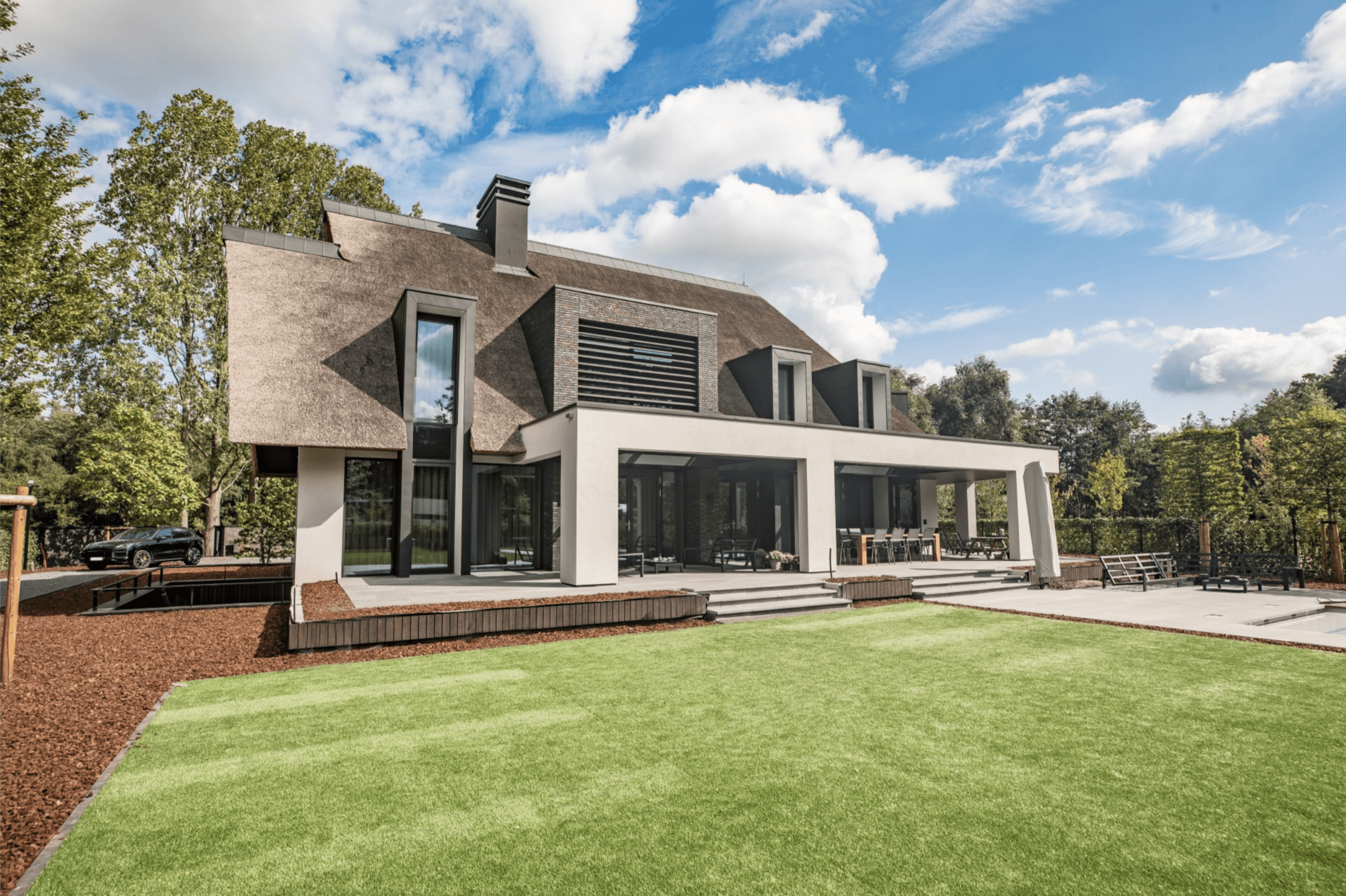 Moderne villa met riet en witte gevel, terras en groen grasveld