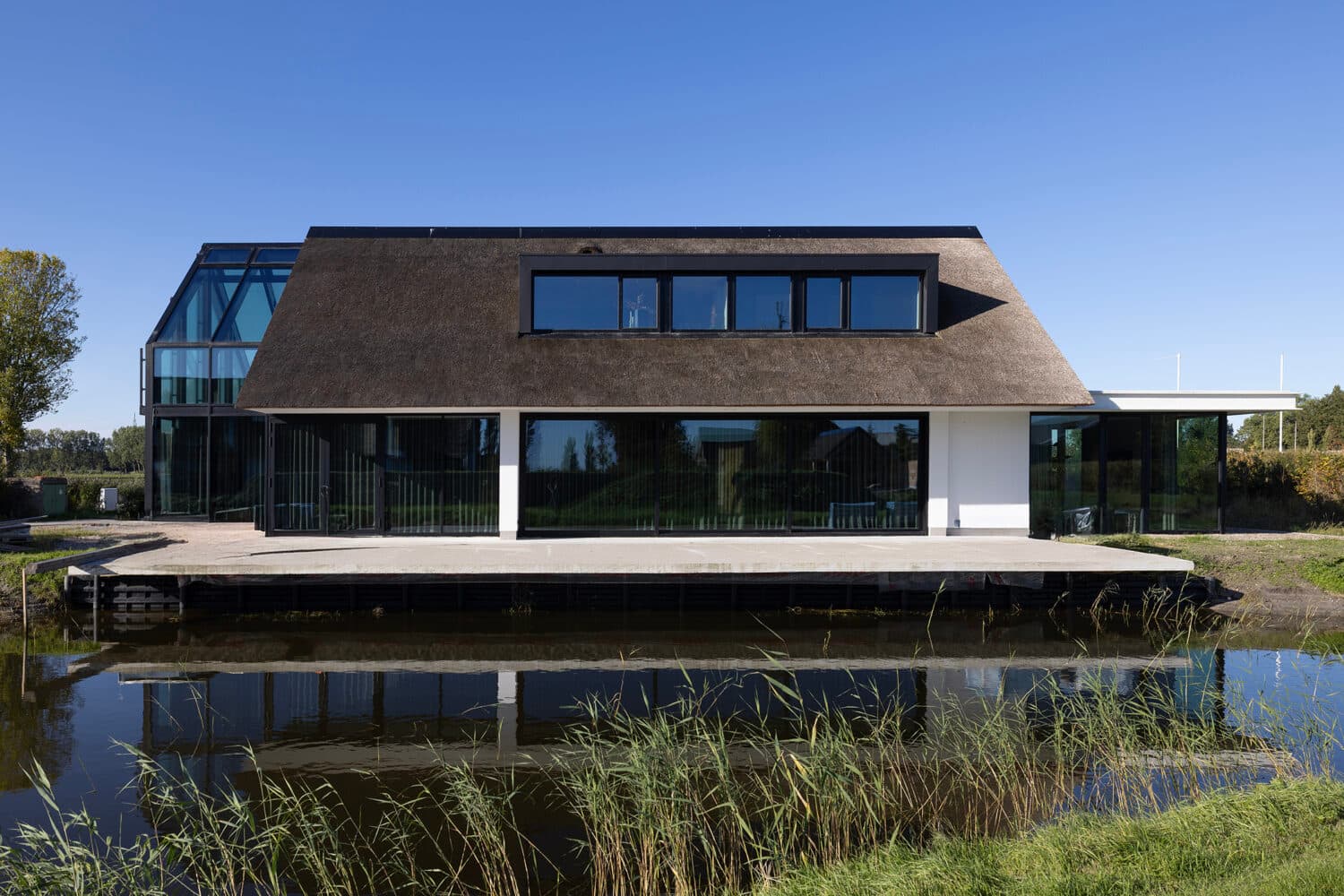 Exterieur woning met rieten dak, grote glaswand en houten berging