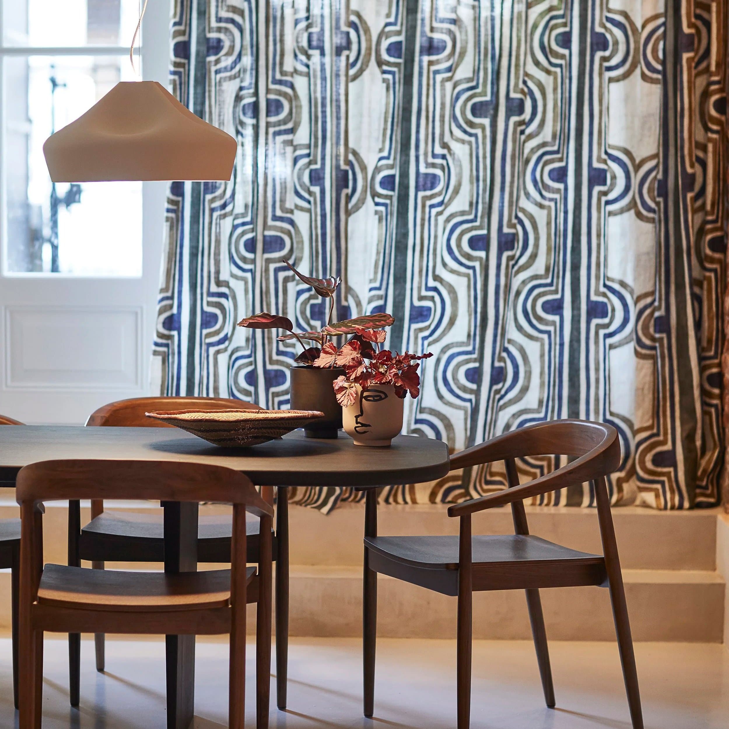 Eetkamer met ronde tafel, houten stoelen en geometrische gordijnen
