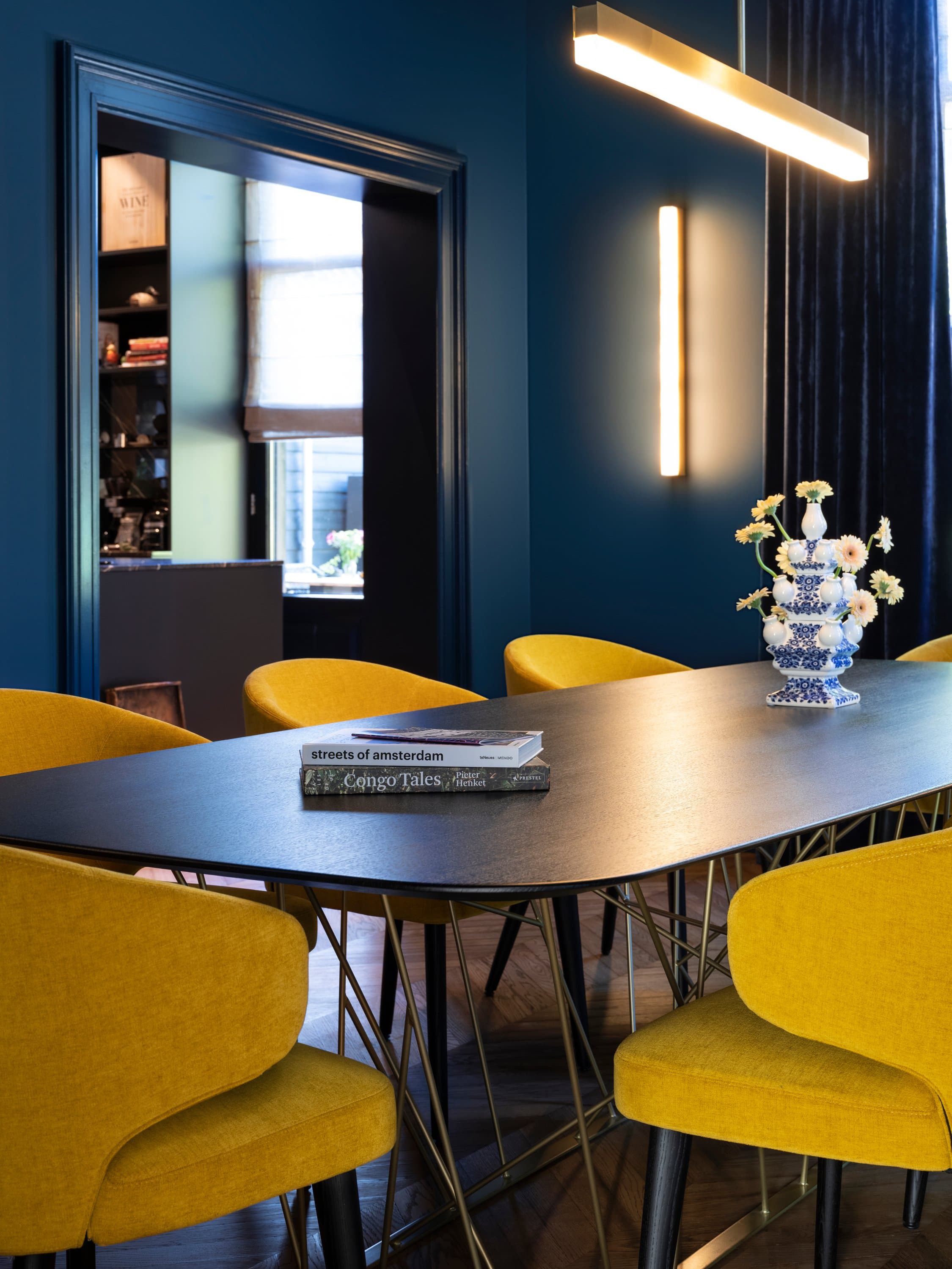 Eetkamer met donkerblauwe wanden, gele stoelen en marmer tafel