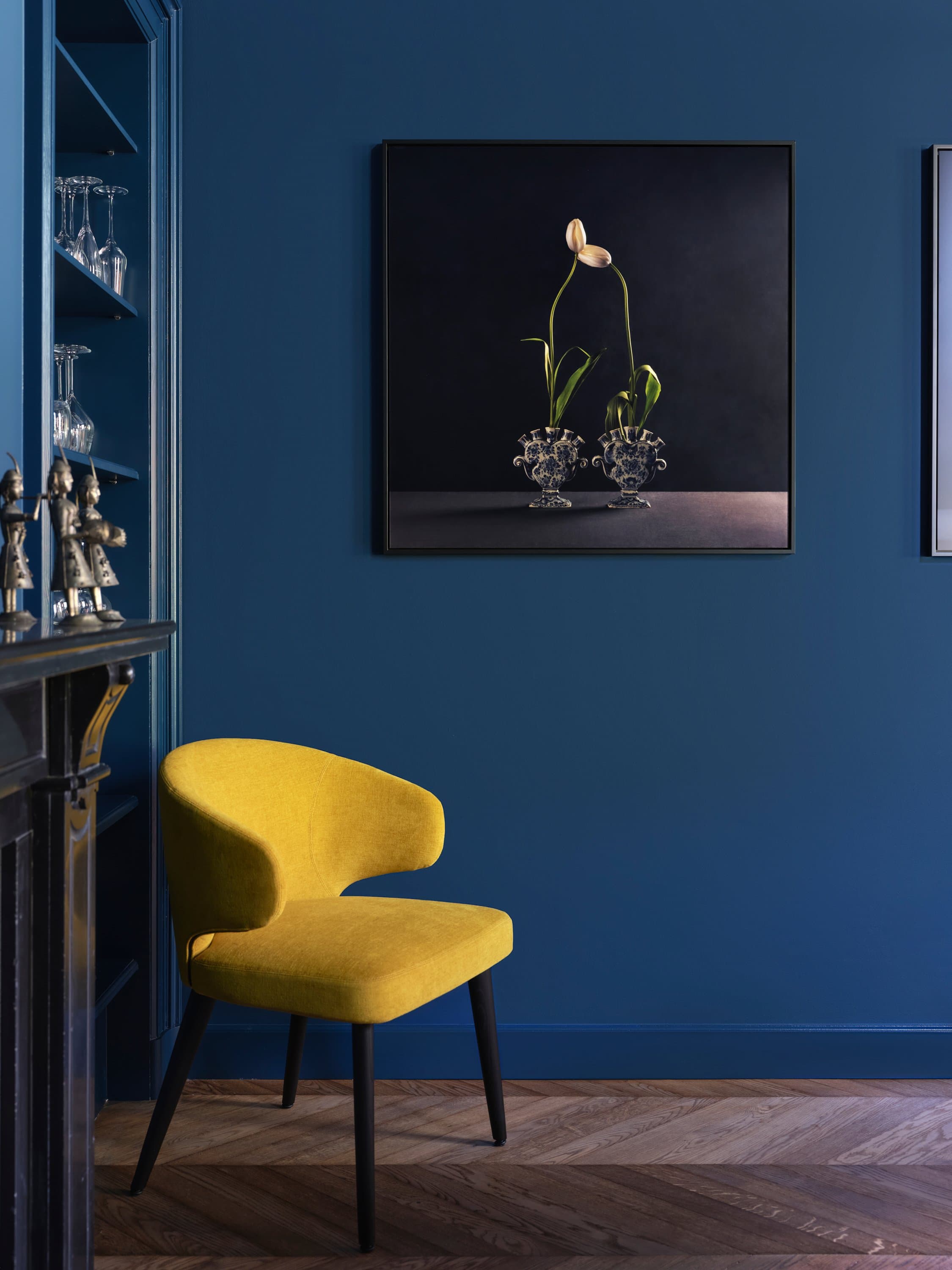 Interieur met donkerblauwe muur, geel fluwelen fauteuil en kunstwerk