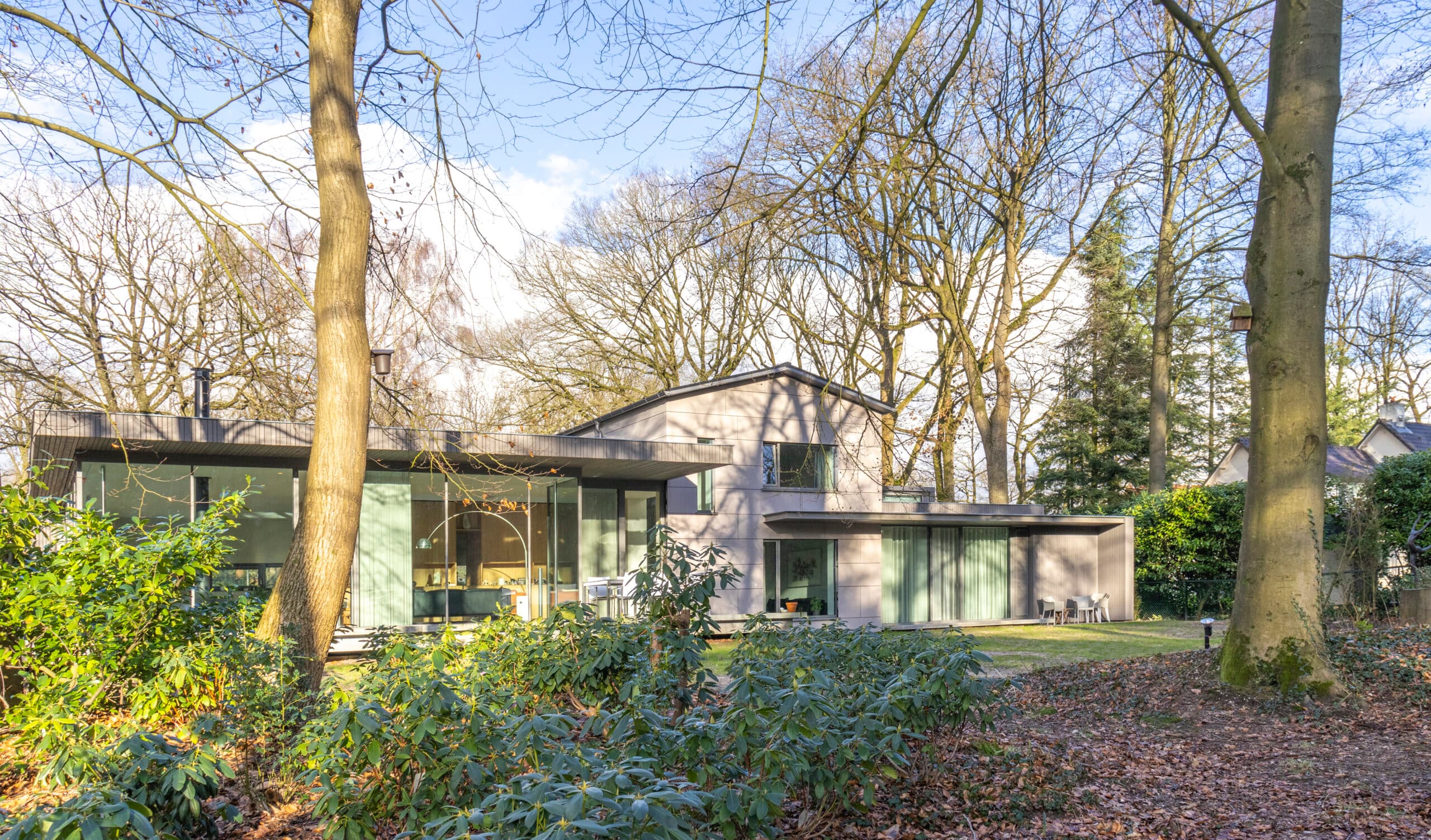 Woning tussen bomen met grijs geveldeel en grote glasvlakken