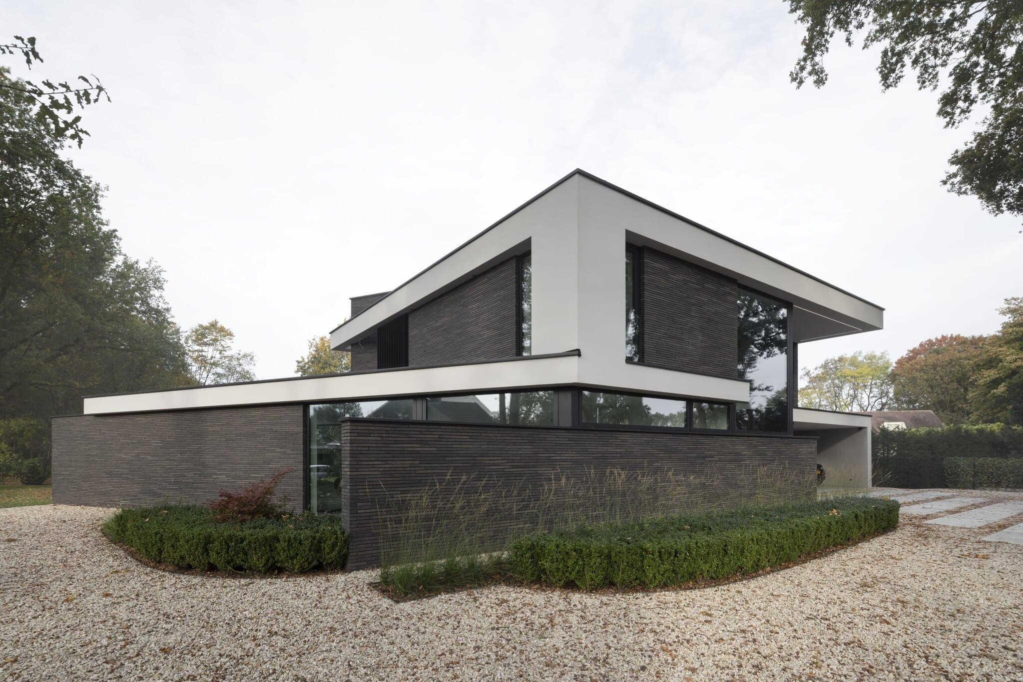 Eigentijdse villa met gestapelde volumes, donkergroene bakstenen en grindpad