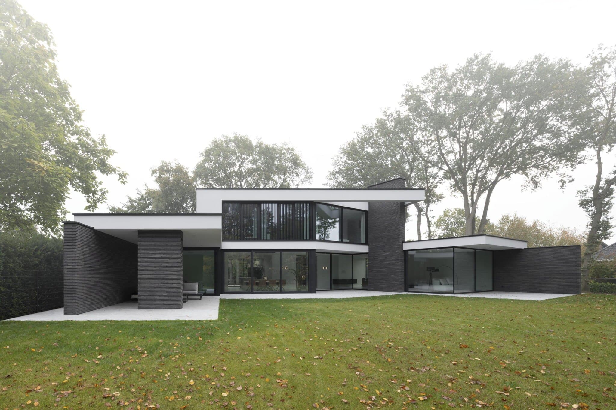Moderne woning met zwarte bakstenen en glazen volumes in landschappelijke setting